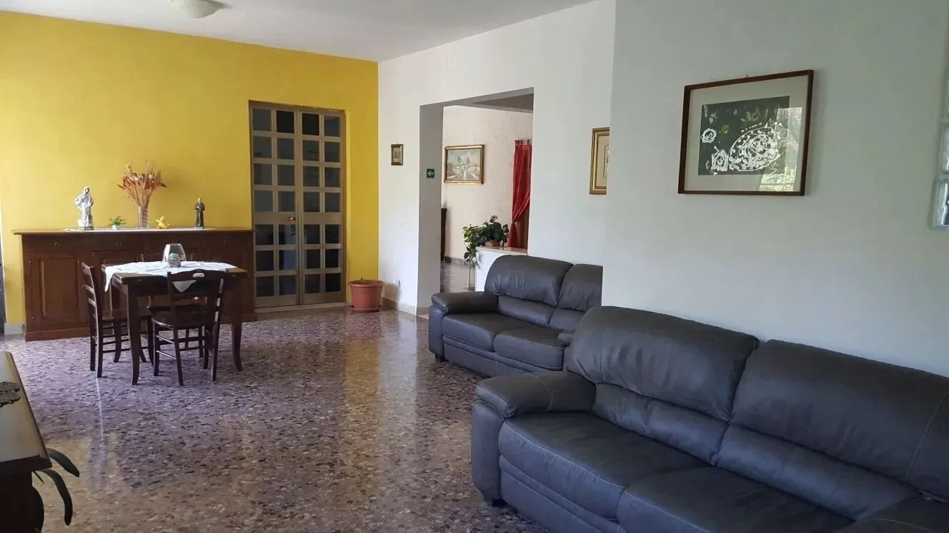 Living room with dark sofas, dining table, yellow accent wall, and a doorway to another room