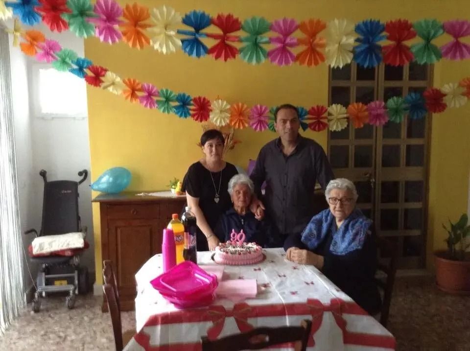 Family gathered around a birthday cake at a decorated table in a yellow-walled room