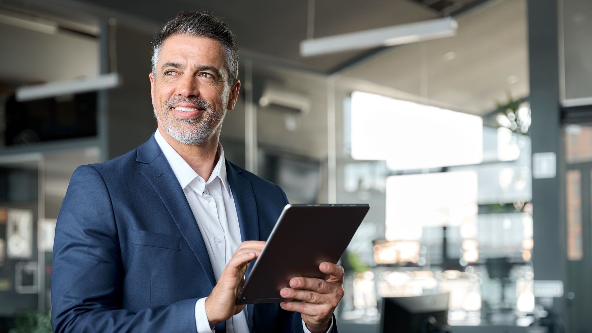 A man in a suit is holding a tablet computer in an office.