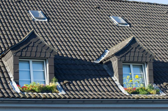 Dormer windows on a gray tiled roof with skylights and flower boxes under the eaves