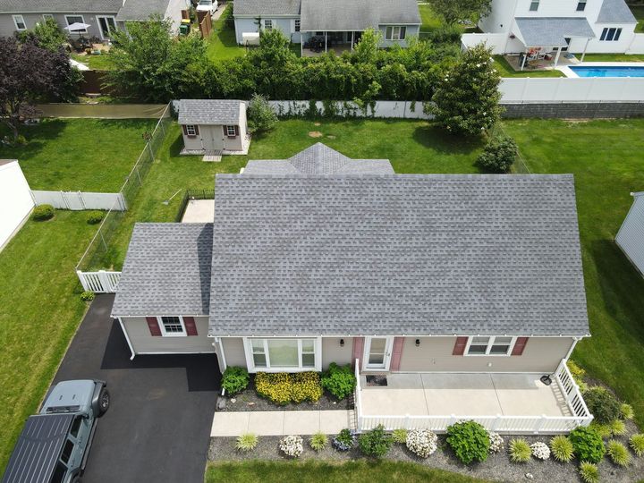 Aerial view of a gray-roofed suburban house with a driveway, lawn, and small front porch