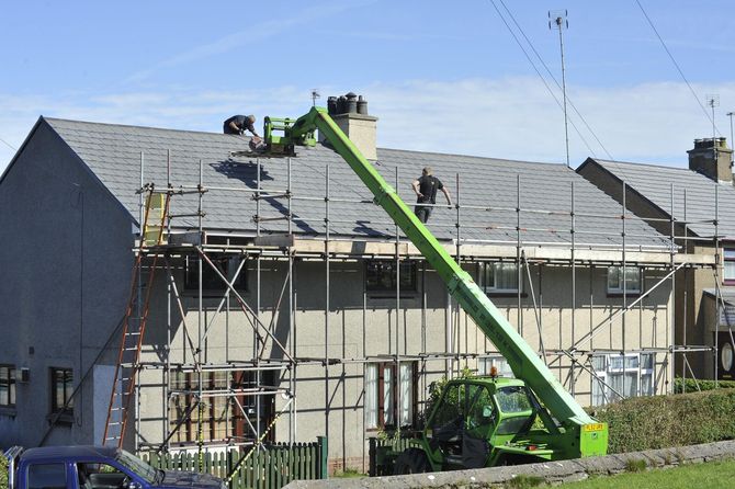 Worker on a green cherry picker repairing a house roof under scaffolding