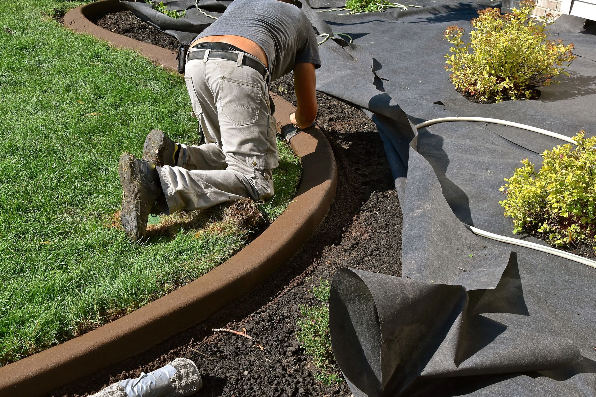 A man is kneeling down to install a lawn edging