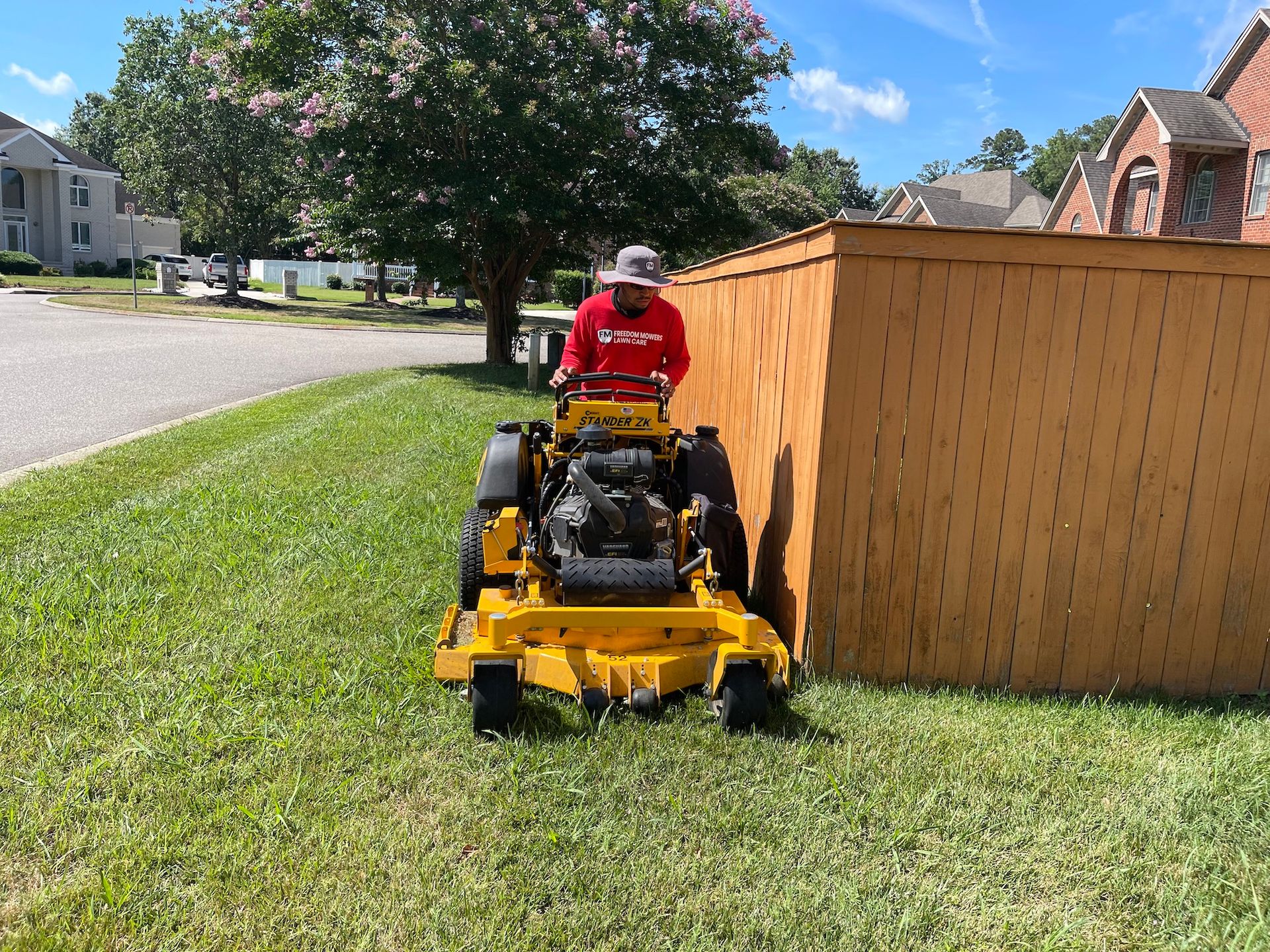 A man is riding a yellow lawn mower next to a wooden fence.