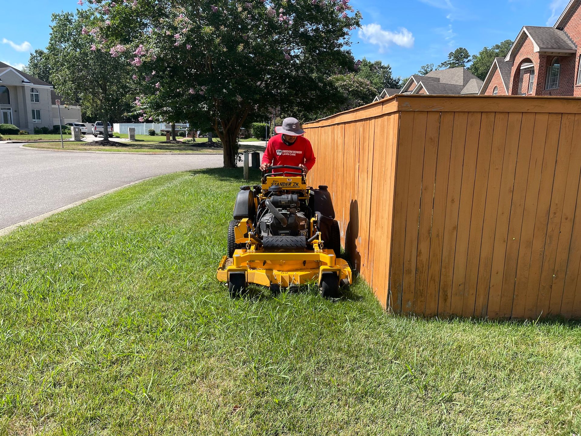 A man is riding a yellow lawn mower next to a wooden fence.