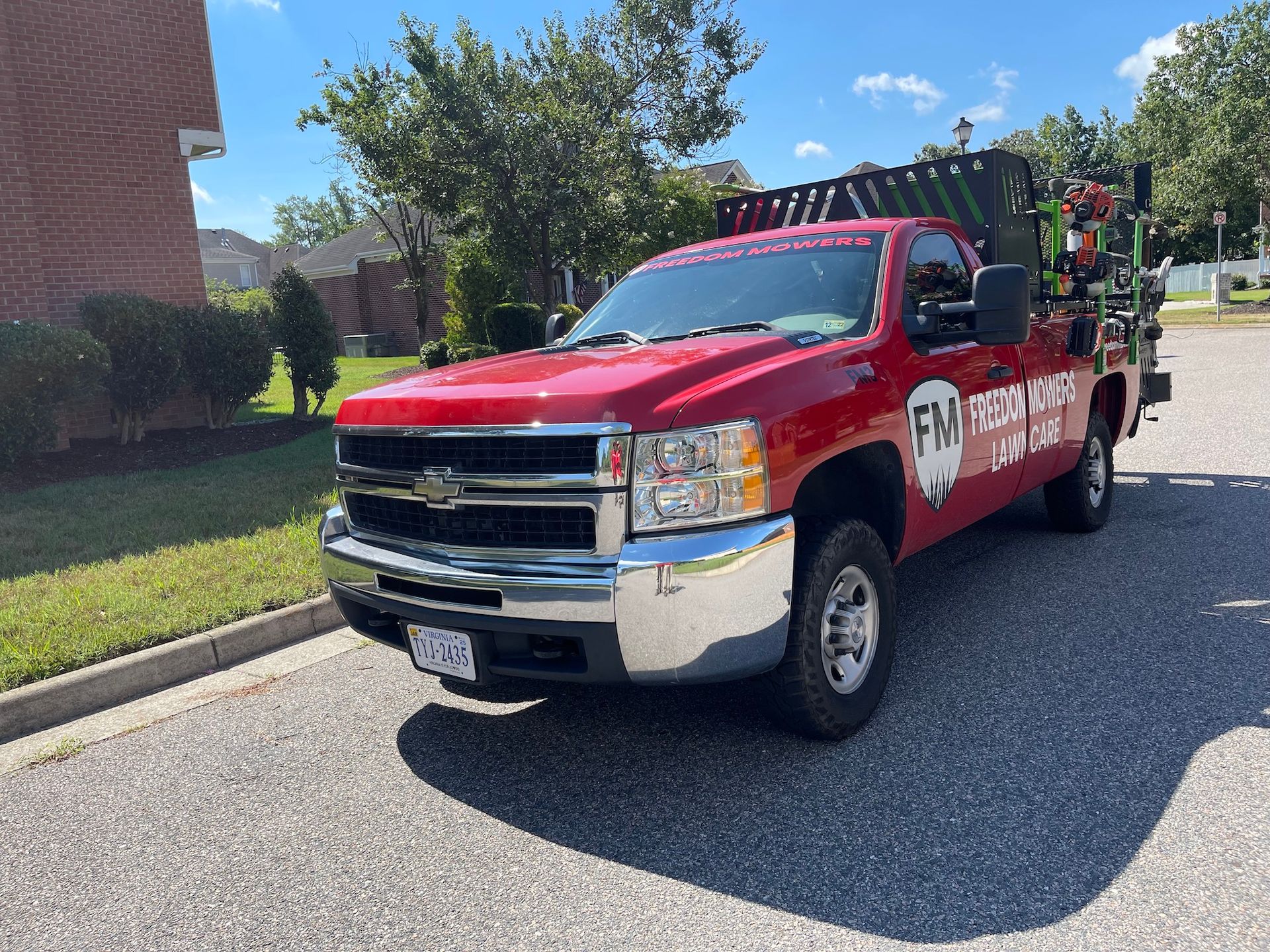 A red truck is parked on the side of the road in front of a brick building.
