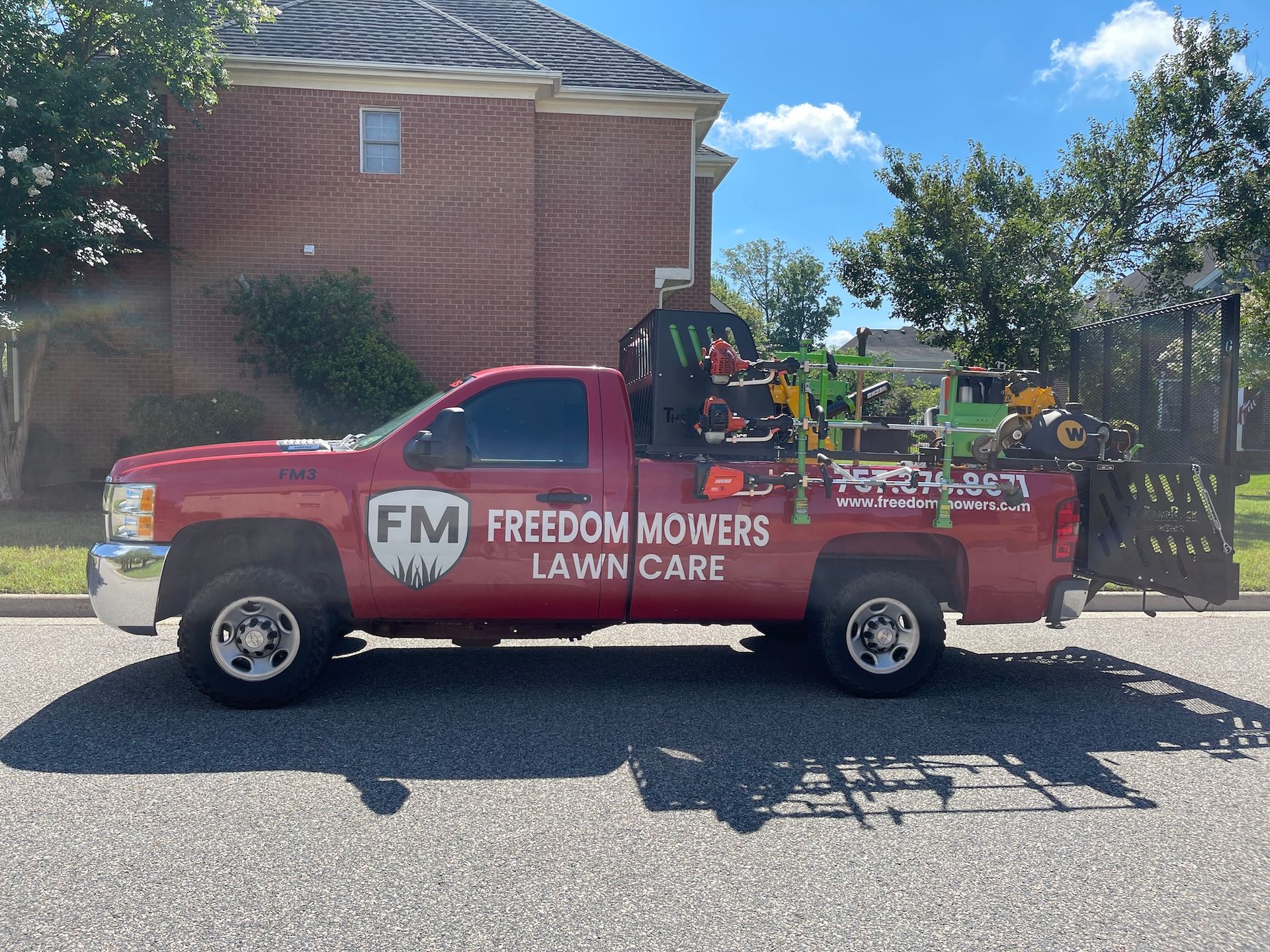 A red freedom mowers lawn care truck is parked in front of a brick house.