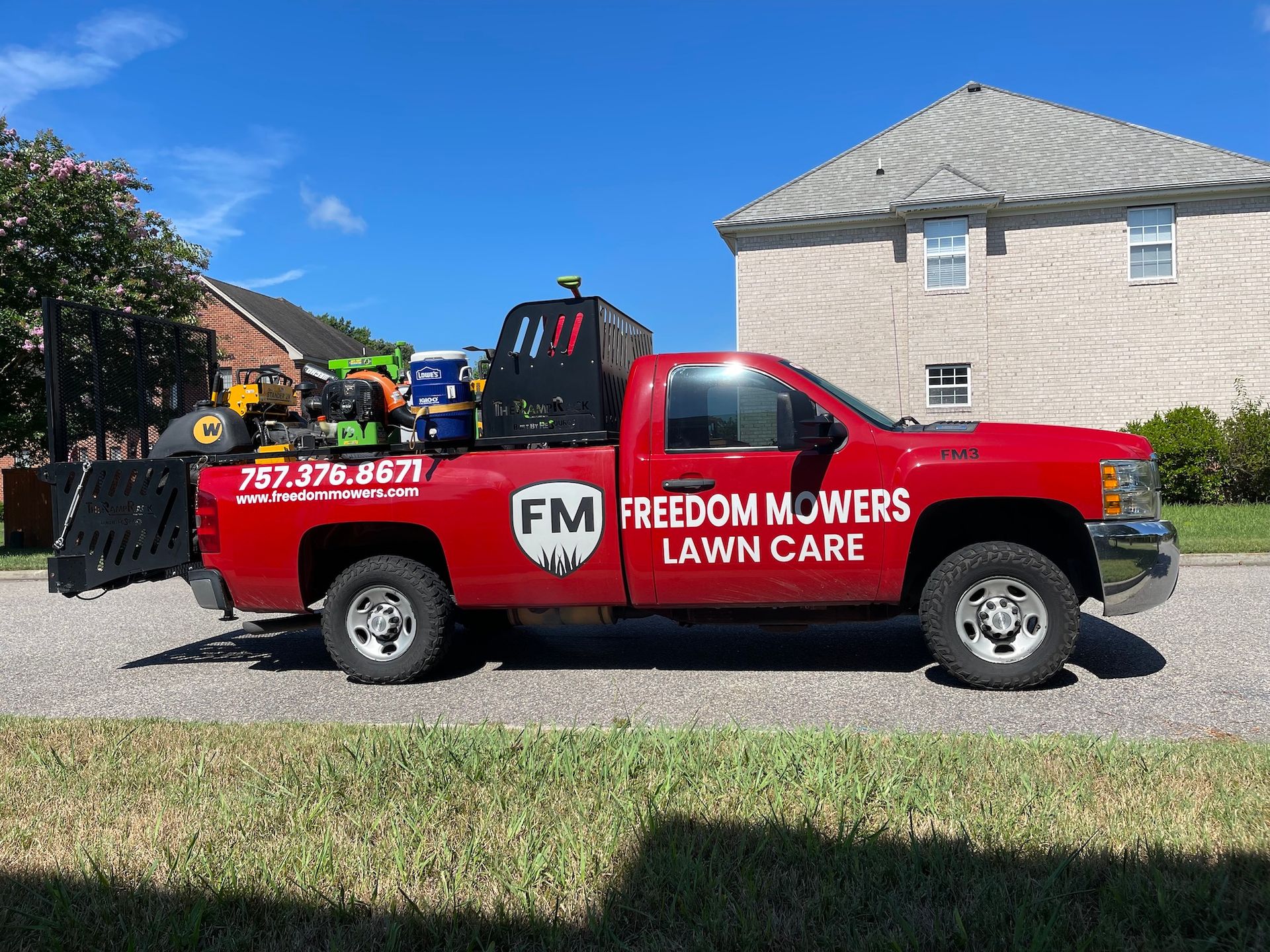 A red freedom mowers lawn care truck is parked in front of a house.