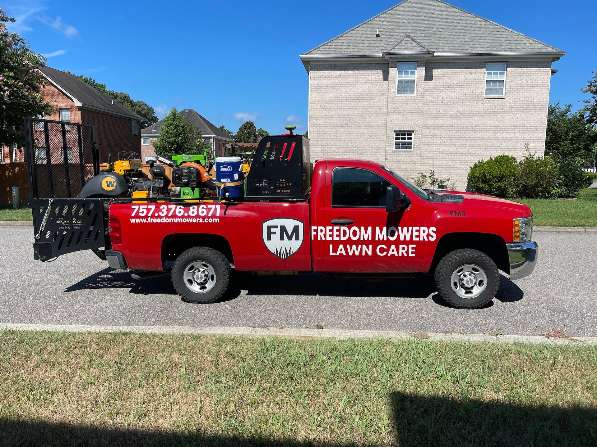 A red freedom mowers lawn care truck is parked in front of a house.