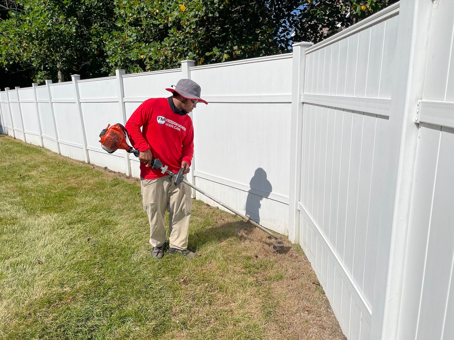 A man is mowing the grass next to a white fence.