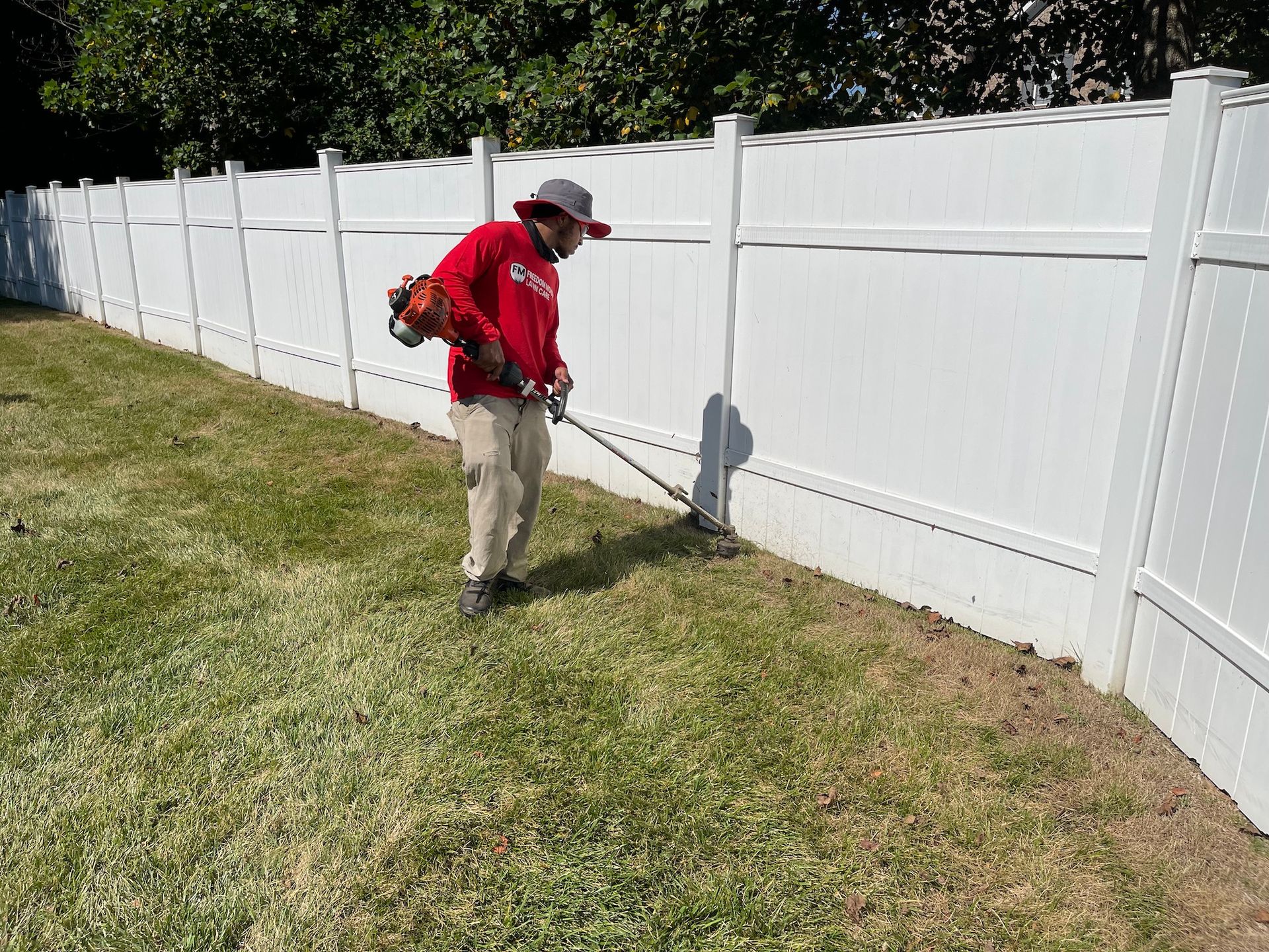 A man is mowing the grass next to a white fence.