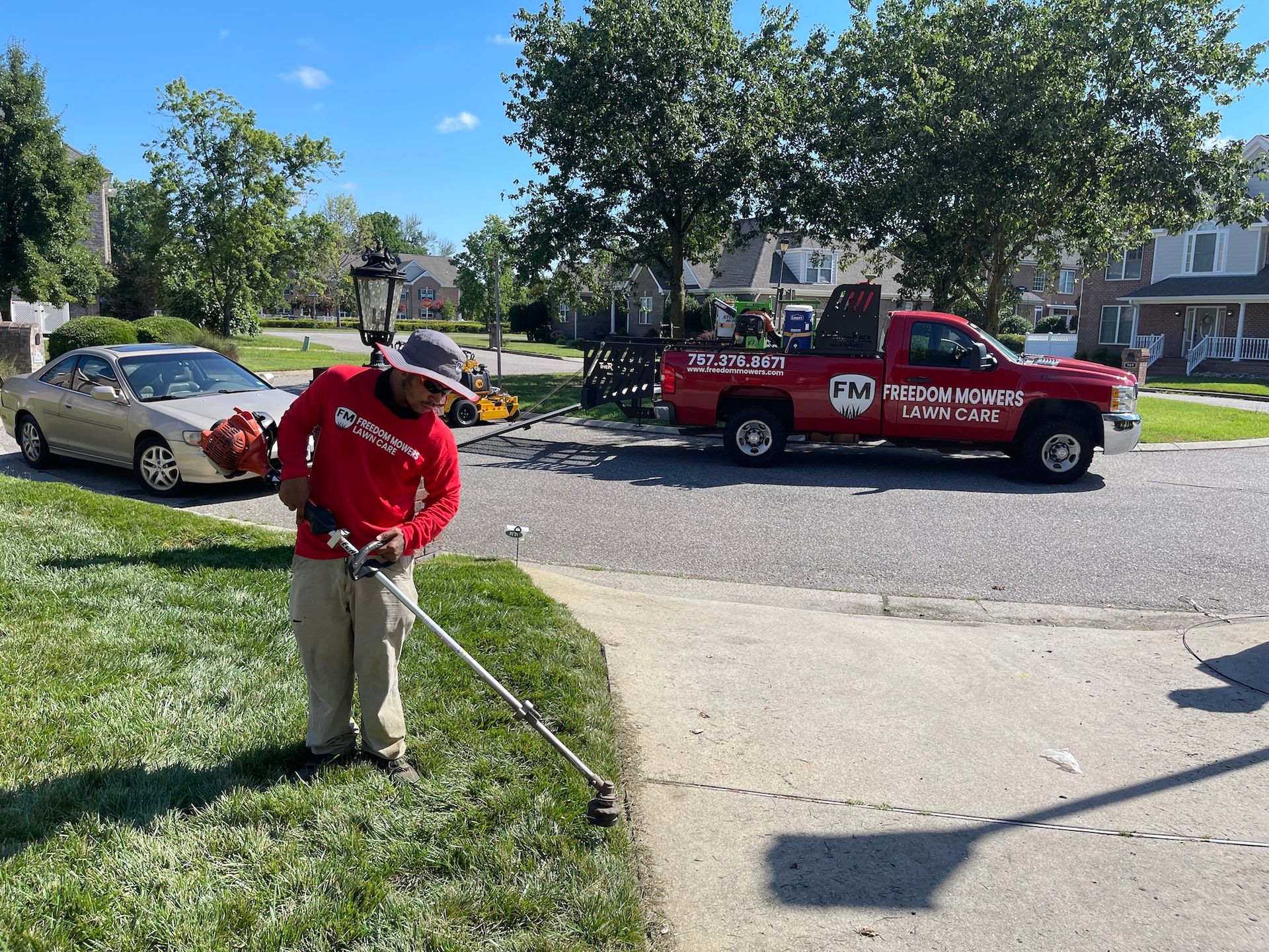 A man is using a lawn mower in front of a red truck.