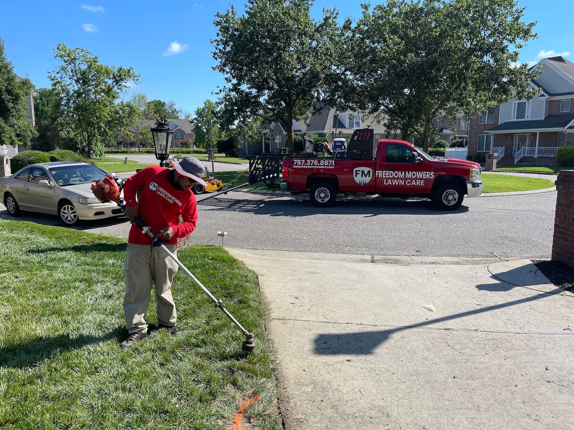 A man is cutting grass in front of a red truck.