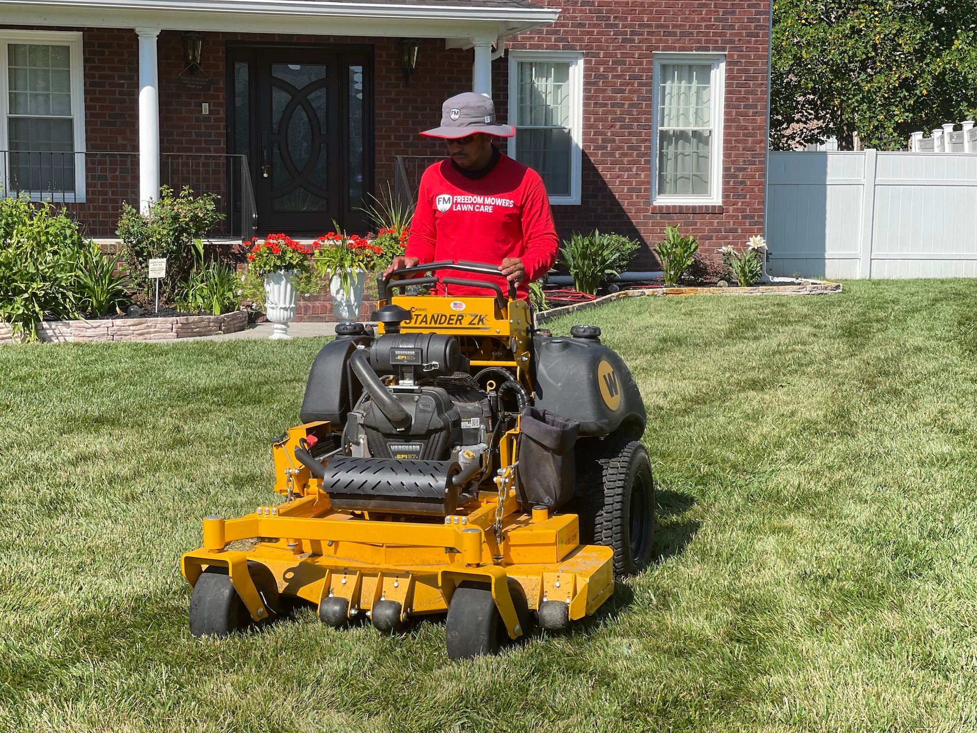 A man is riding a yellow lawn mower in front of a brick house.