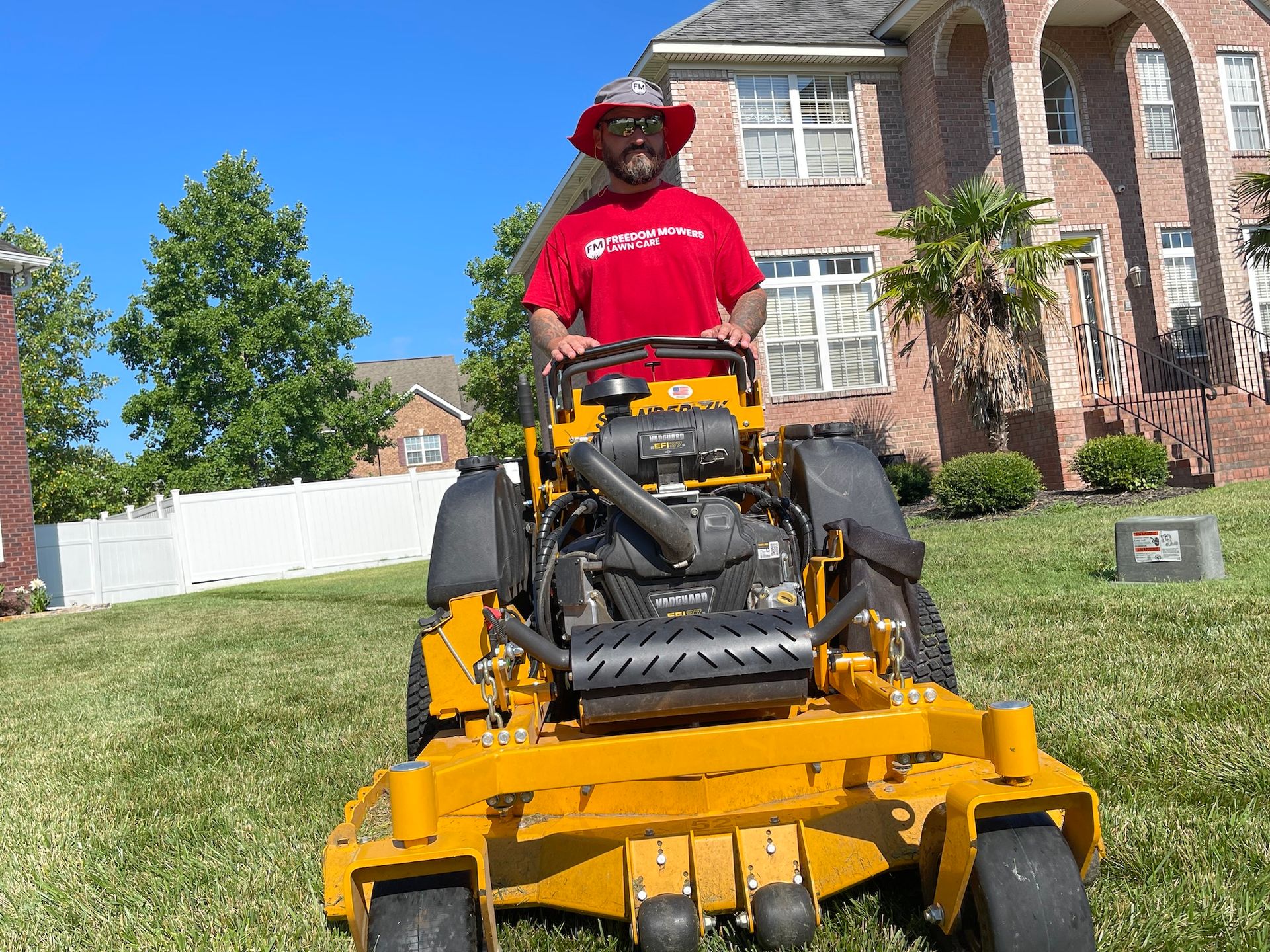 A man is riding a yellow lawn mower in front of a brick house.