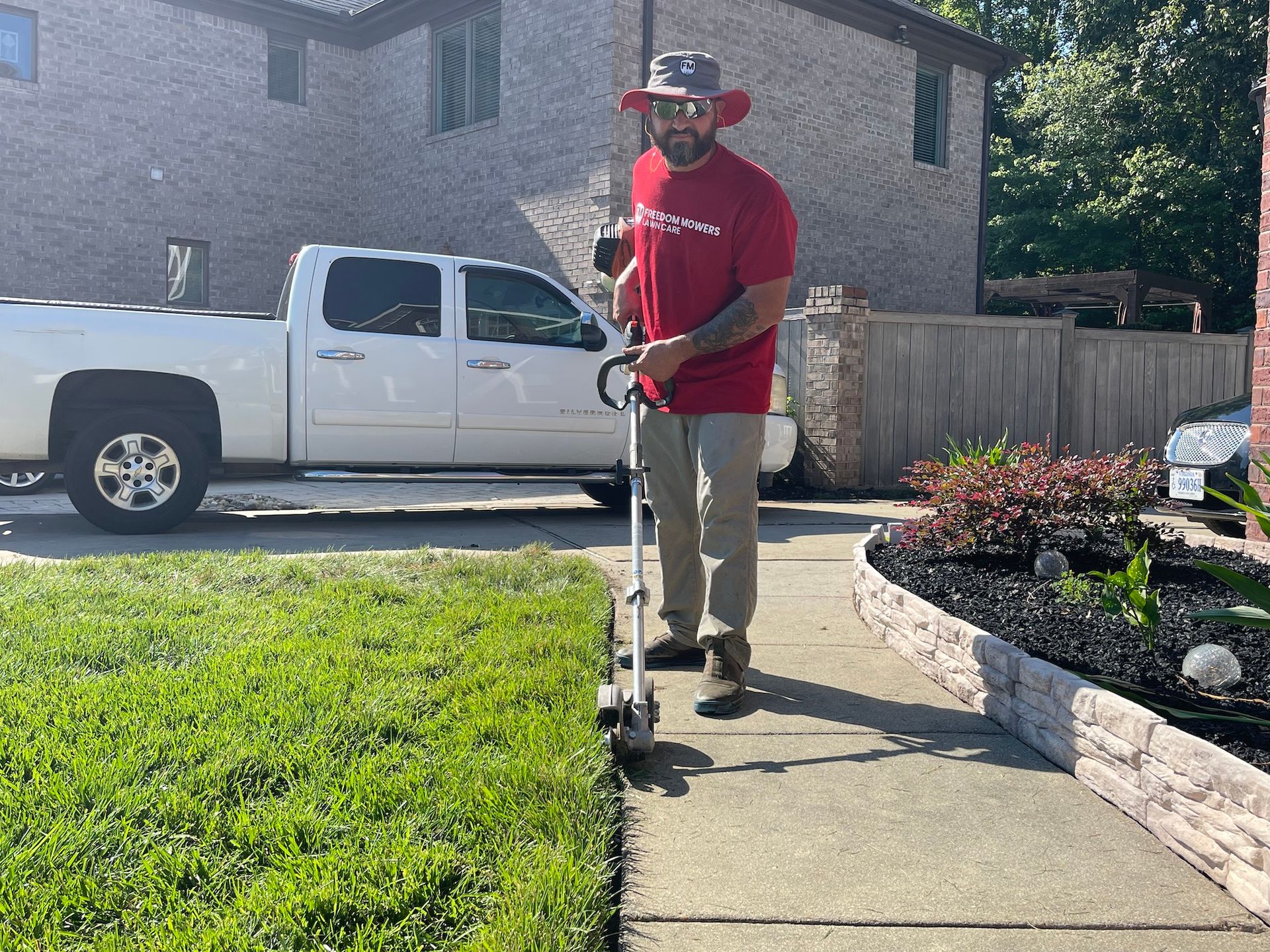 A man is standing on a sidewalk holding a lawn mower.