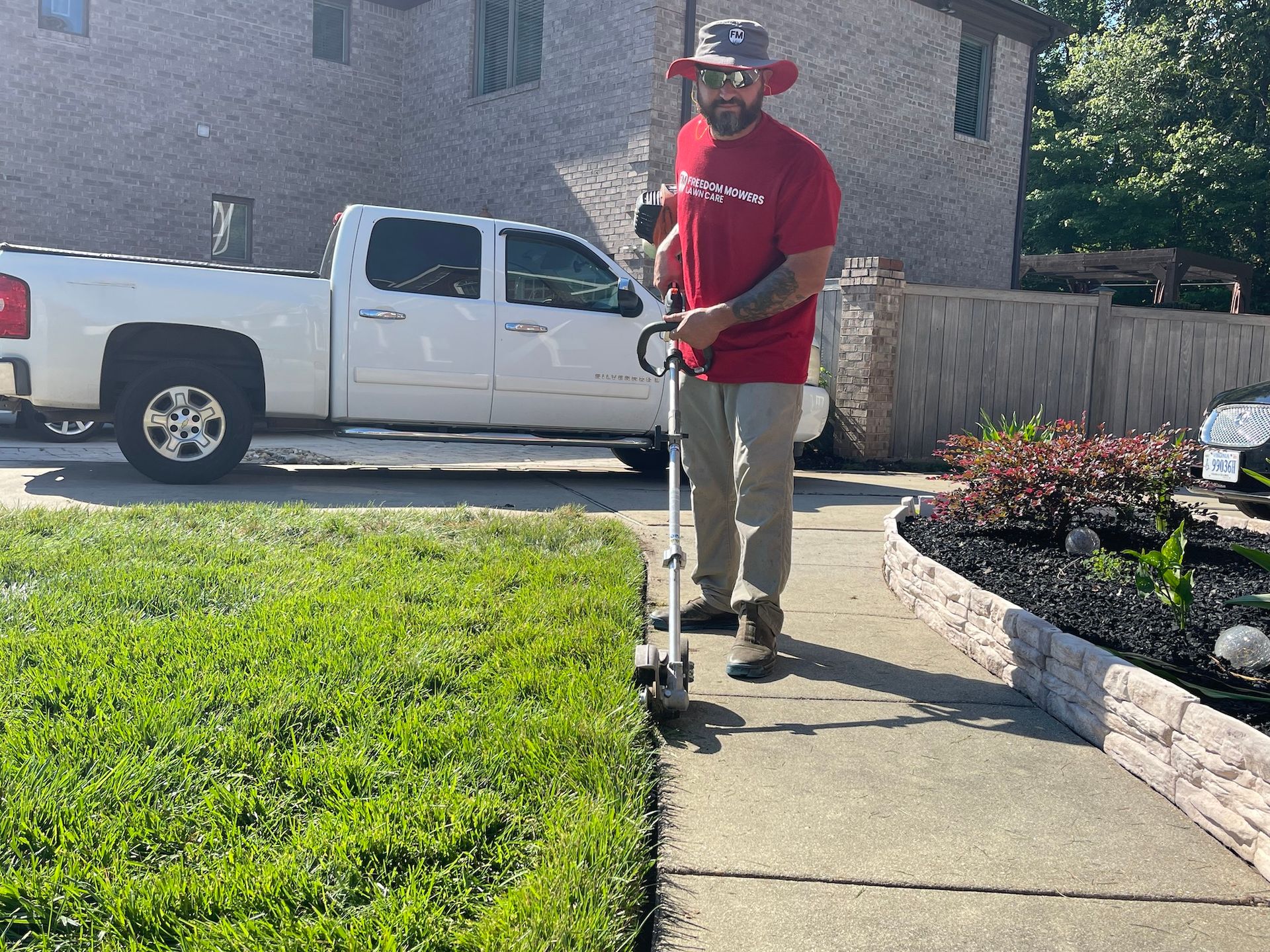 A man is standing on a sidewalk using a lawn mower.