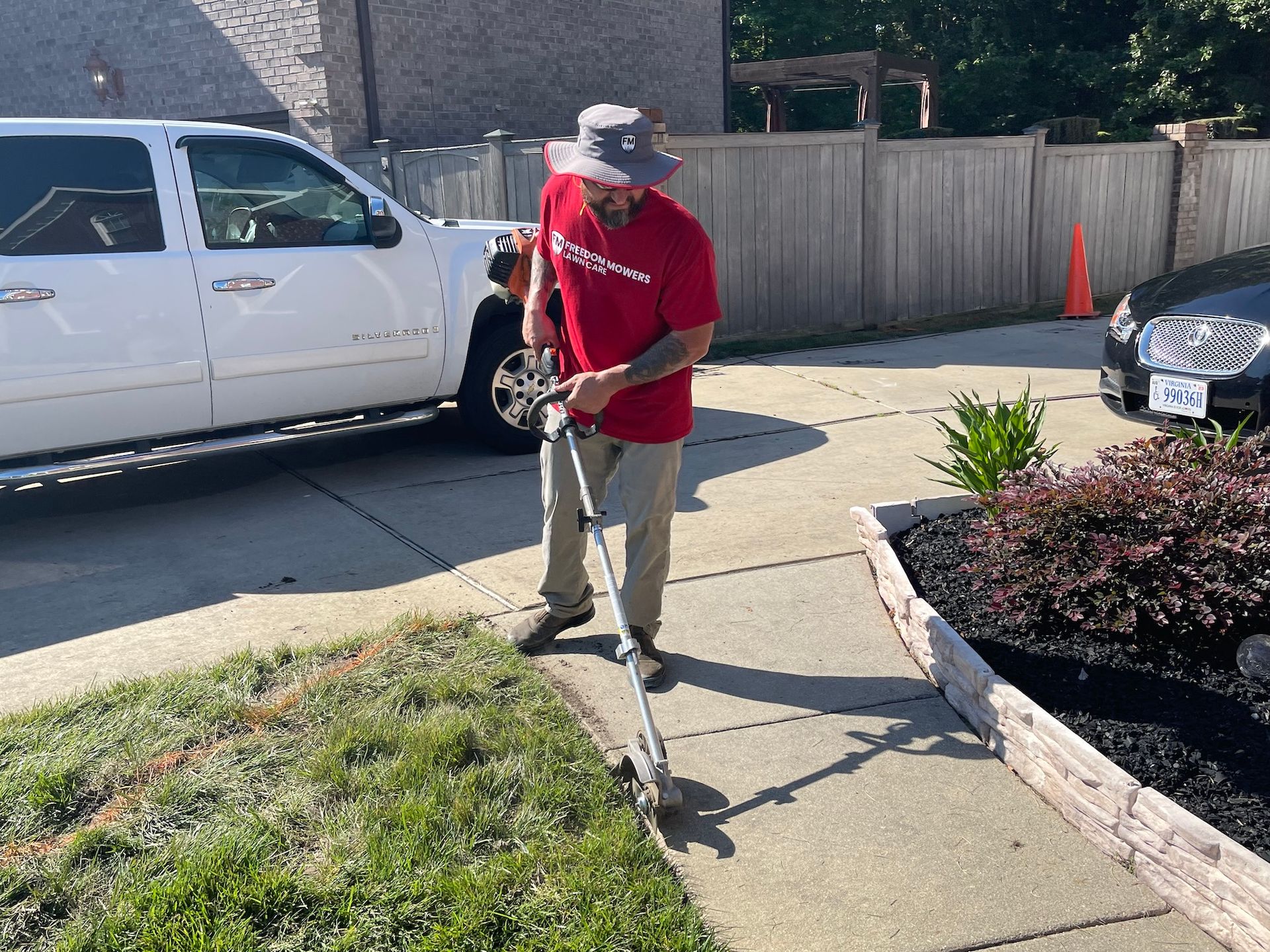 A man in a red shirt is using a lawn mower on a sidewalk.
