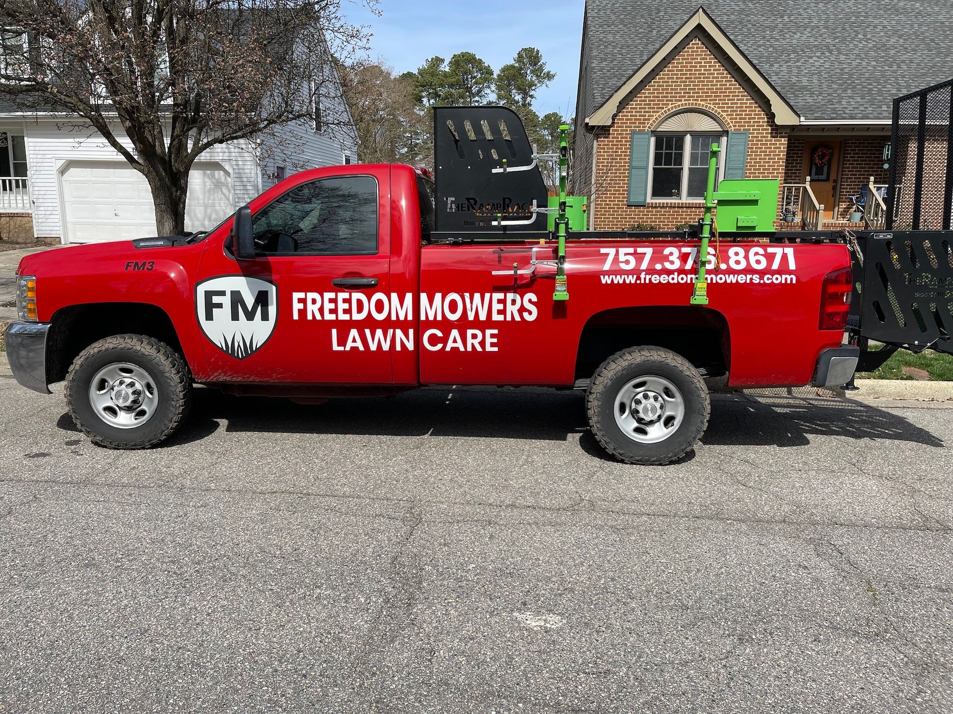 A red freedom mowers lawn care truck is parked in front of a house.
