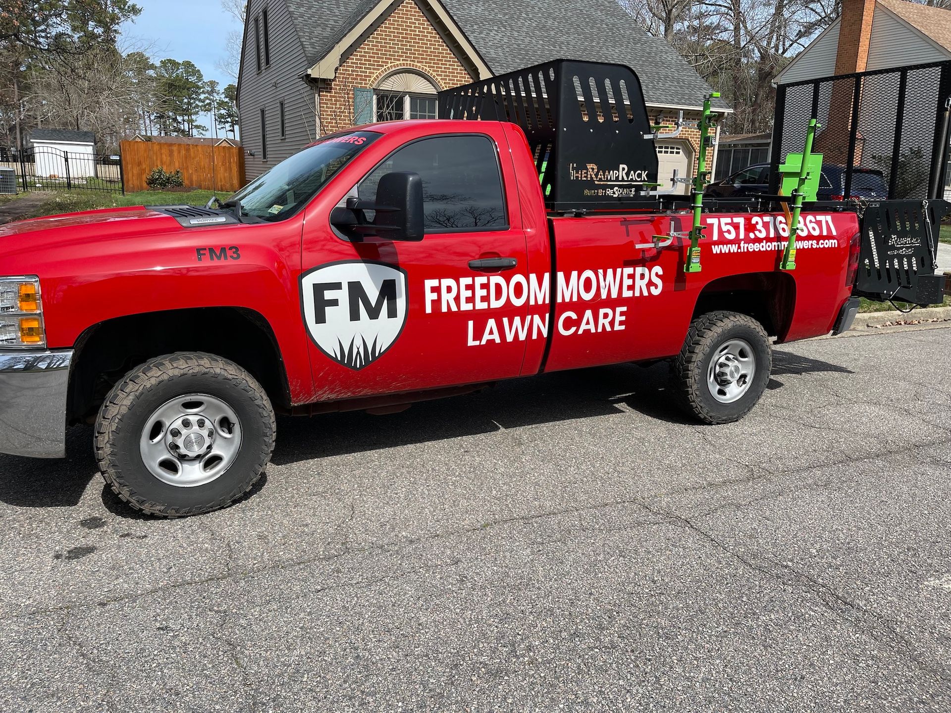 A red freedom mowers lawn care truck is parked in front of a house.