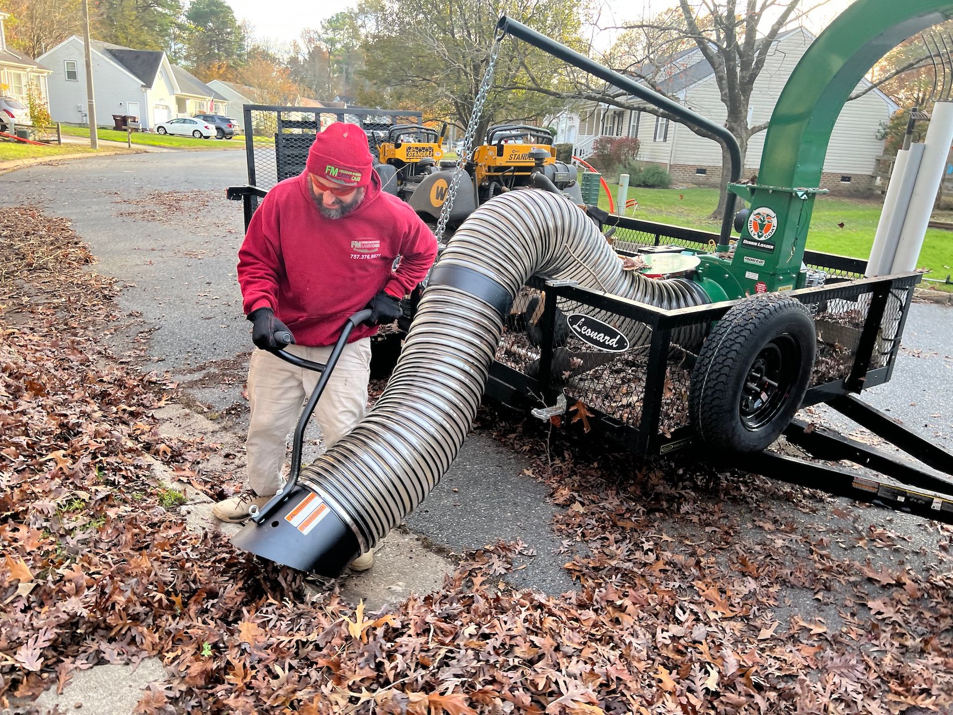 A man is blowing leaves from a trailer with a hose attached to it.