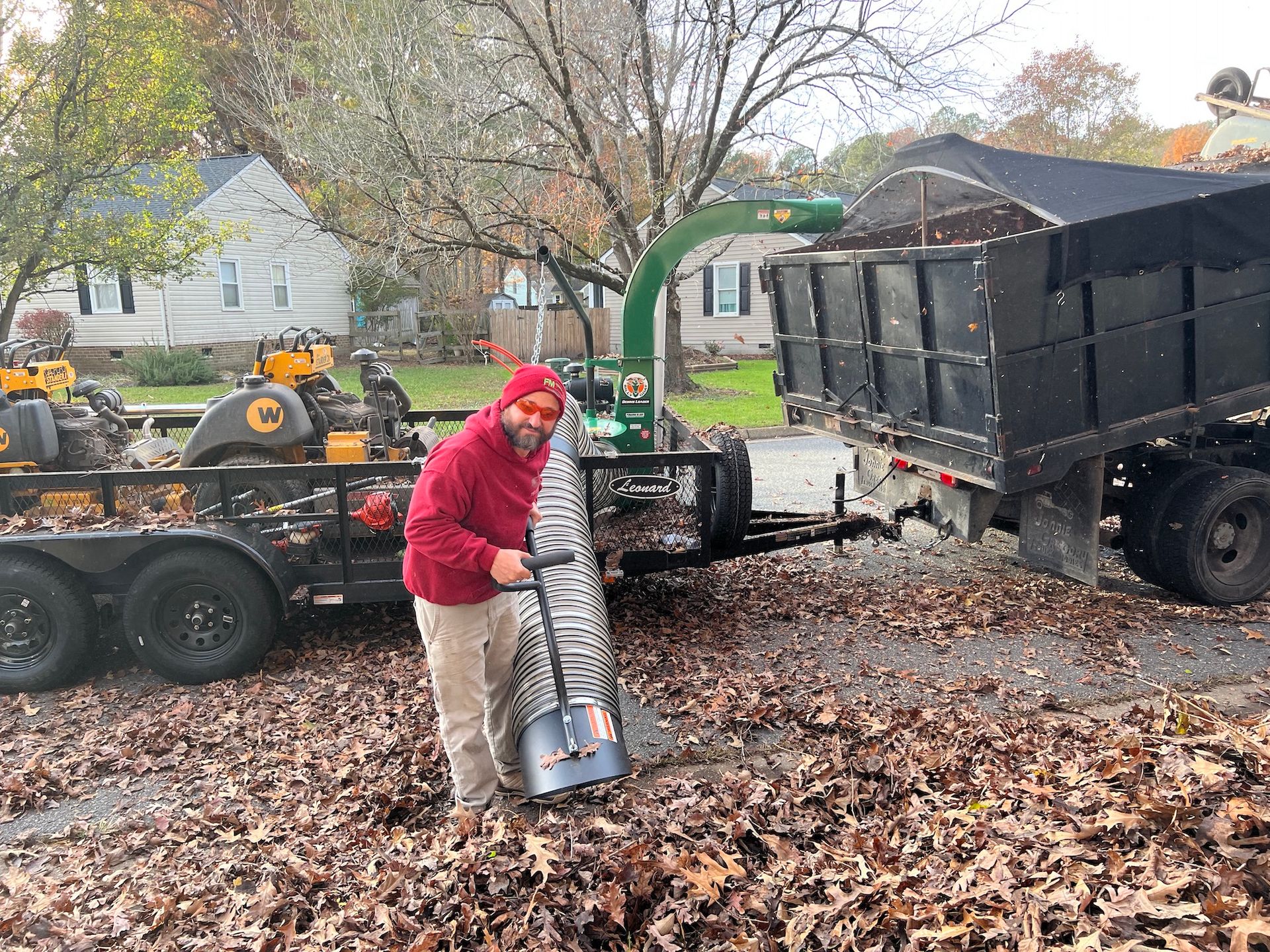 A man is raking leaves in front of a dump truck.