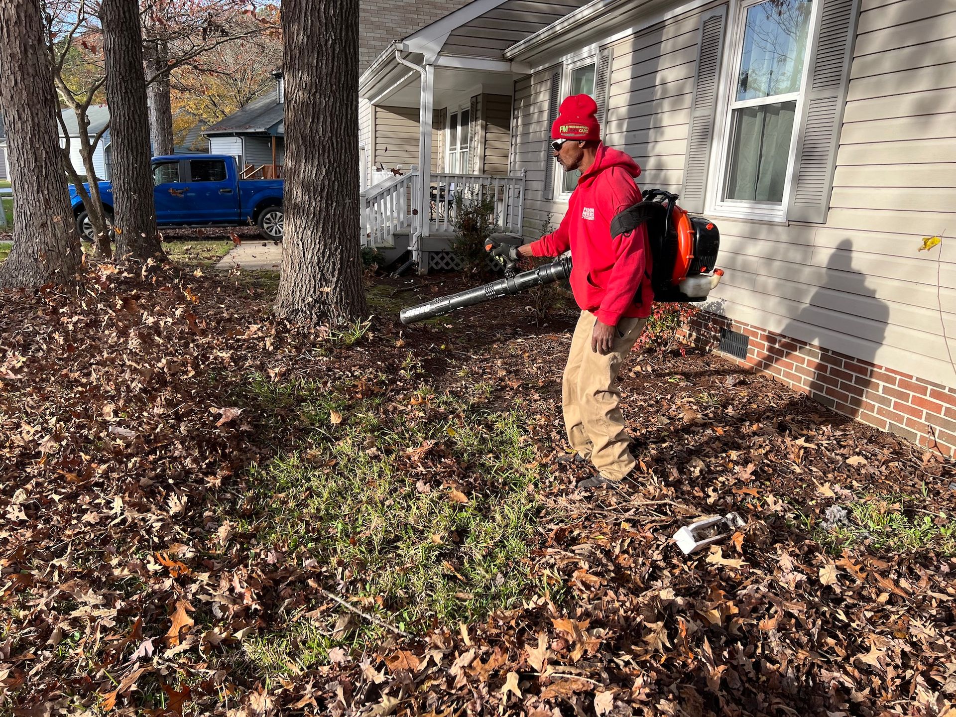 A man is blowing leaves in front of a house.