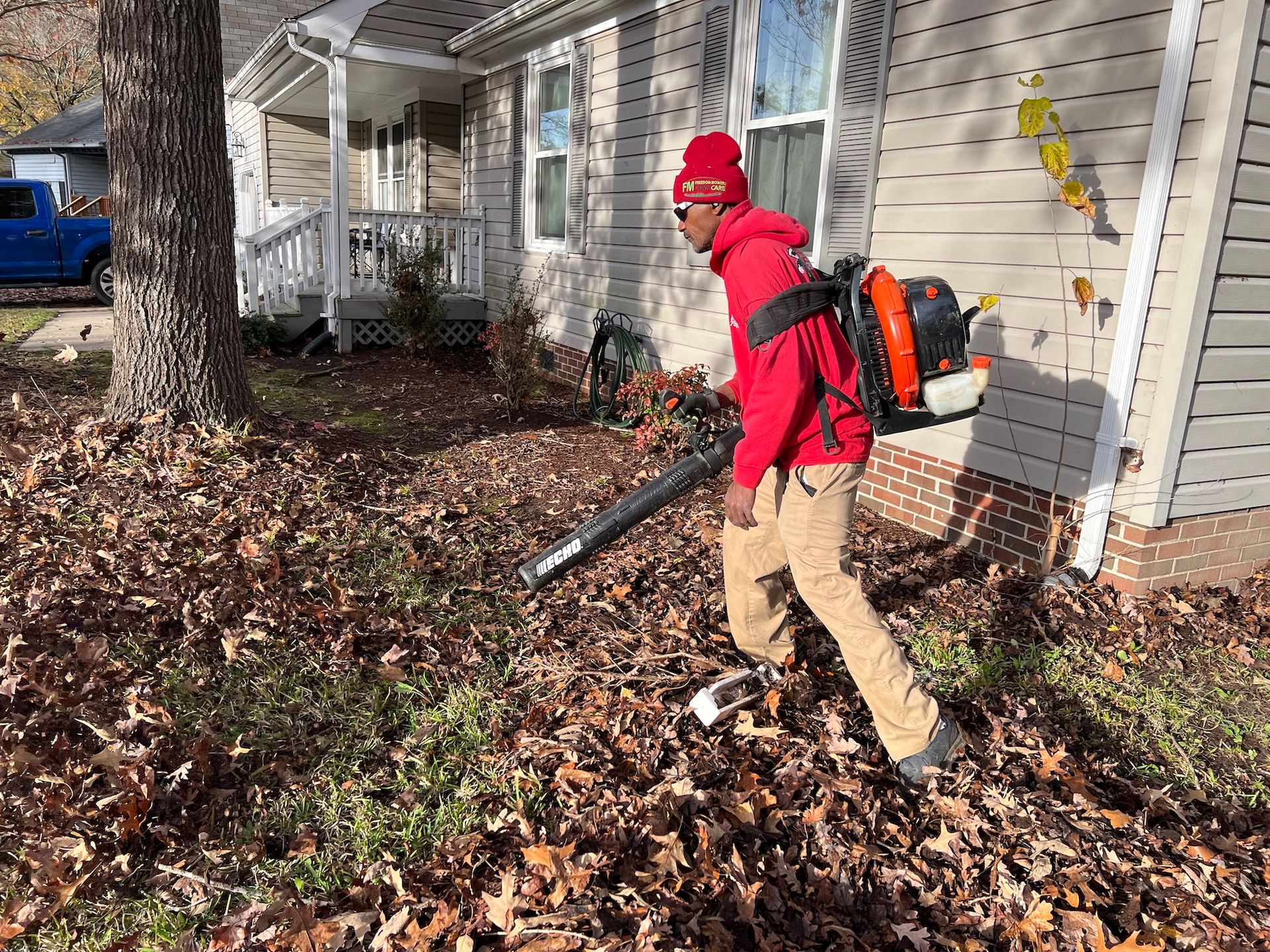 A man is blowing leaves in front of a house.