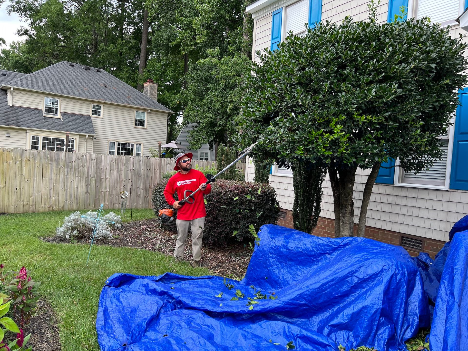 A man is cutting a tree in front of a house with a blue tarp.