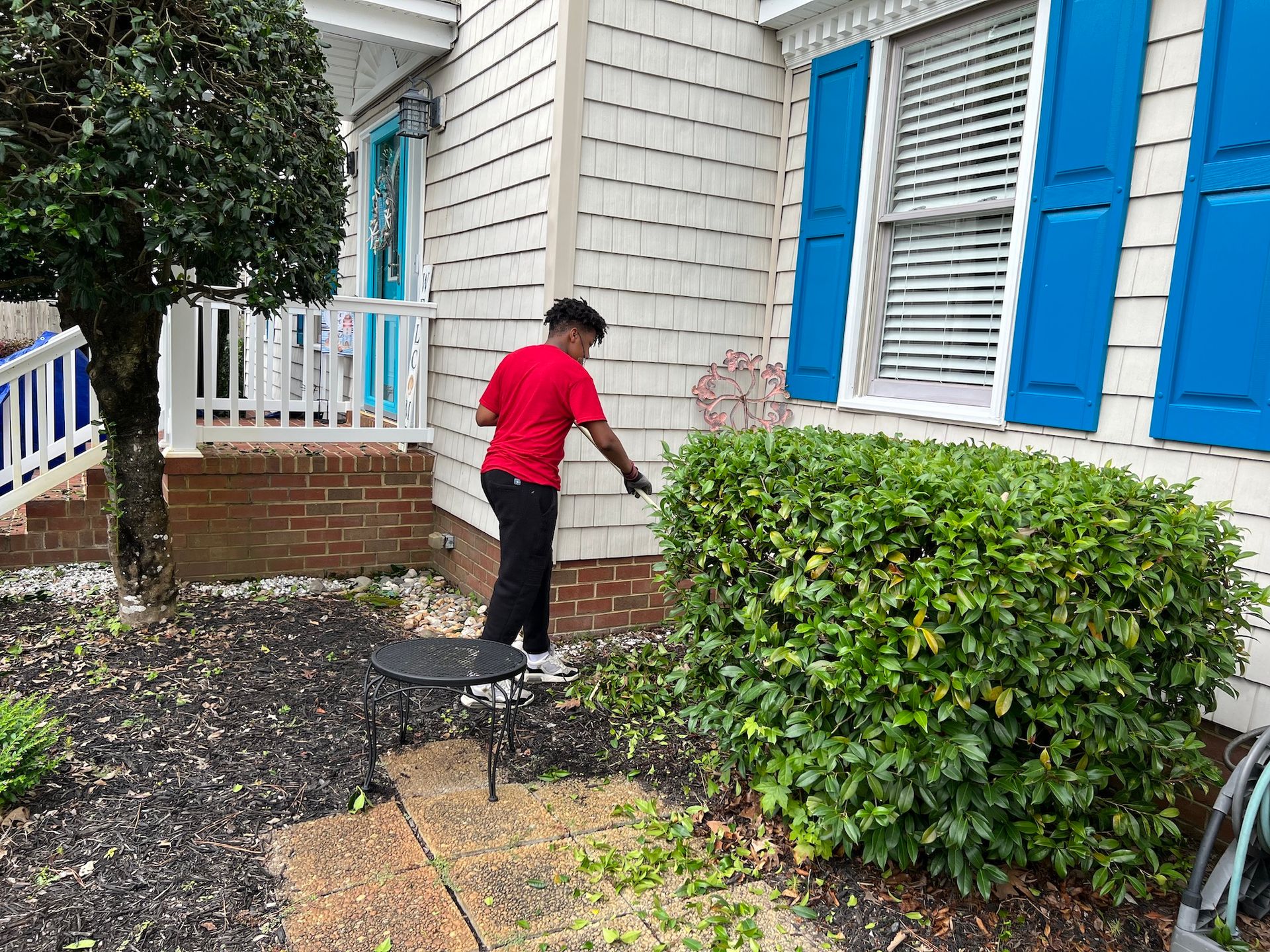 A woman is standing in front of a white house with blue shutters.