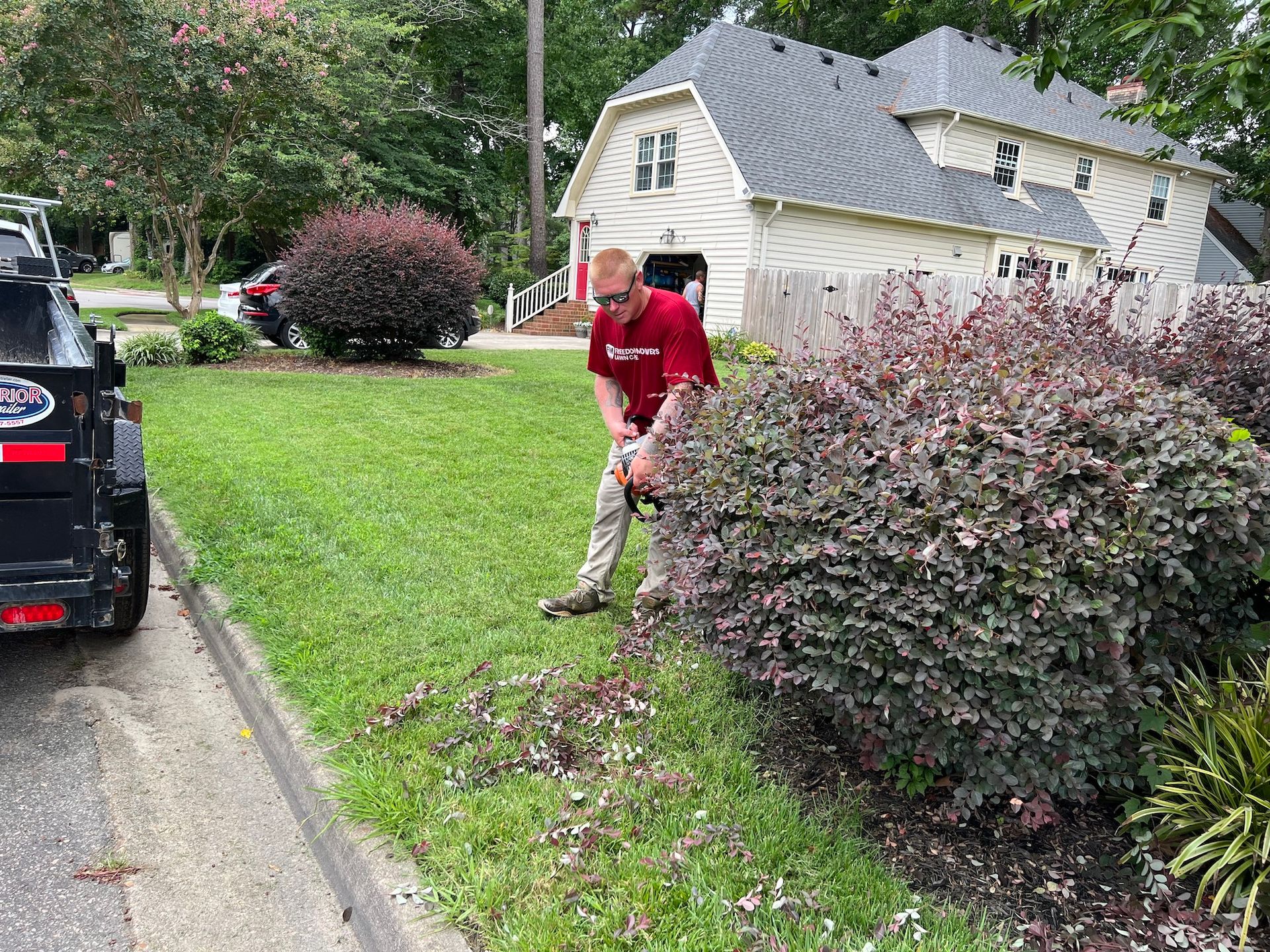 A man is cutting a bush with a lawn mower in front of a house.
