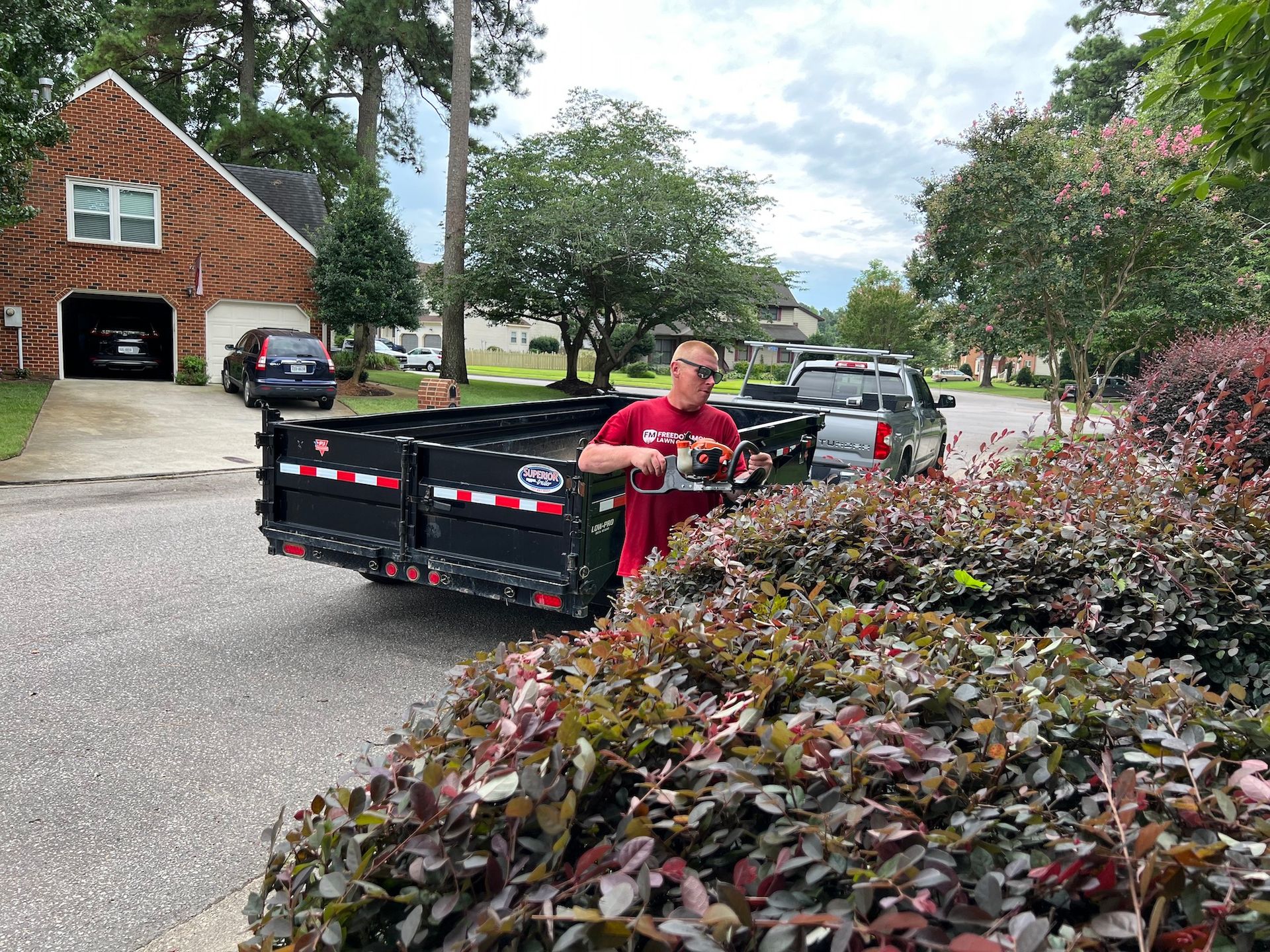 A man is driving a dumpster down a street in front of a house.