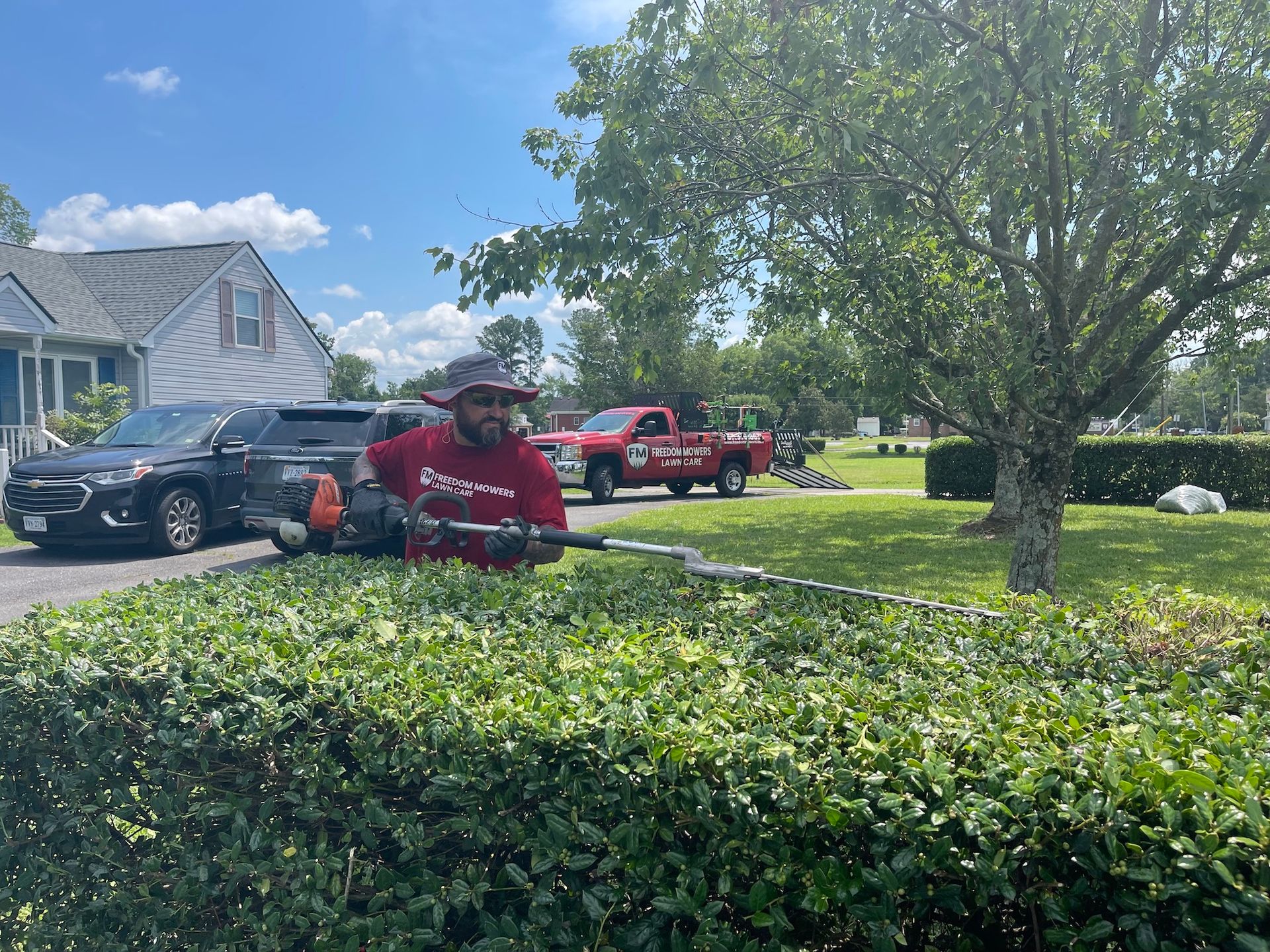 A man is cutting a hedge with a hedge trimmer in front of a house.