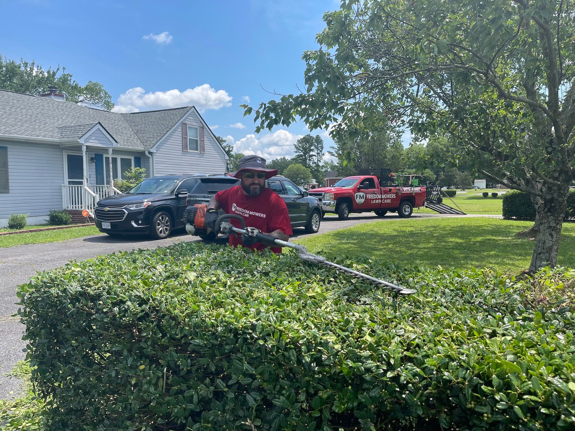 A man is cutting a hedge with a hedge trimmer in front of a house.