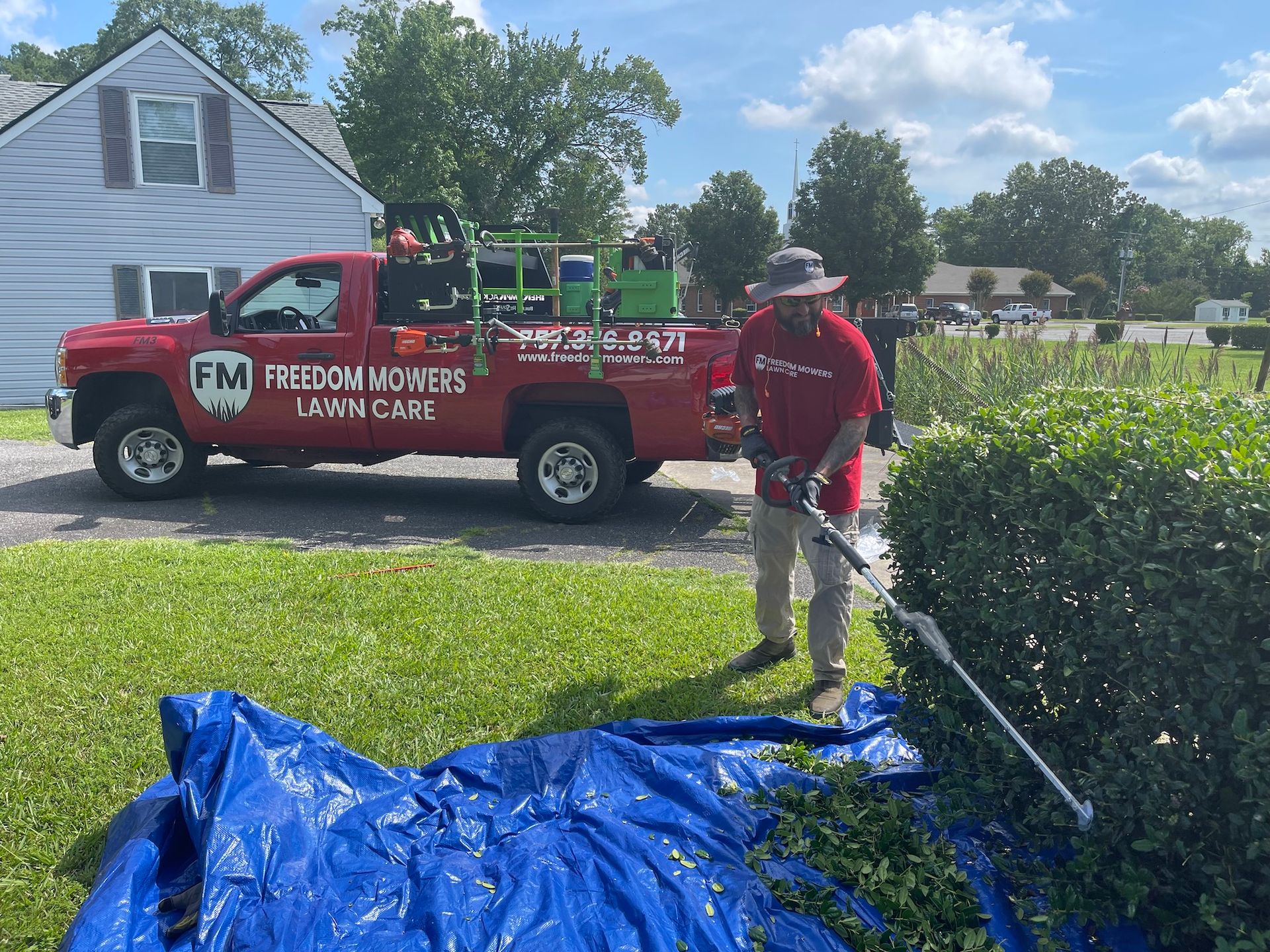 A man is cutting a bush in front of a red truck.