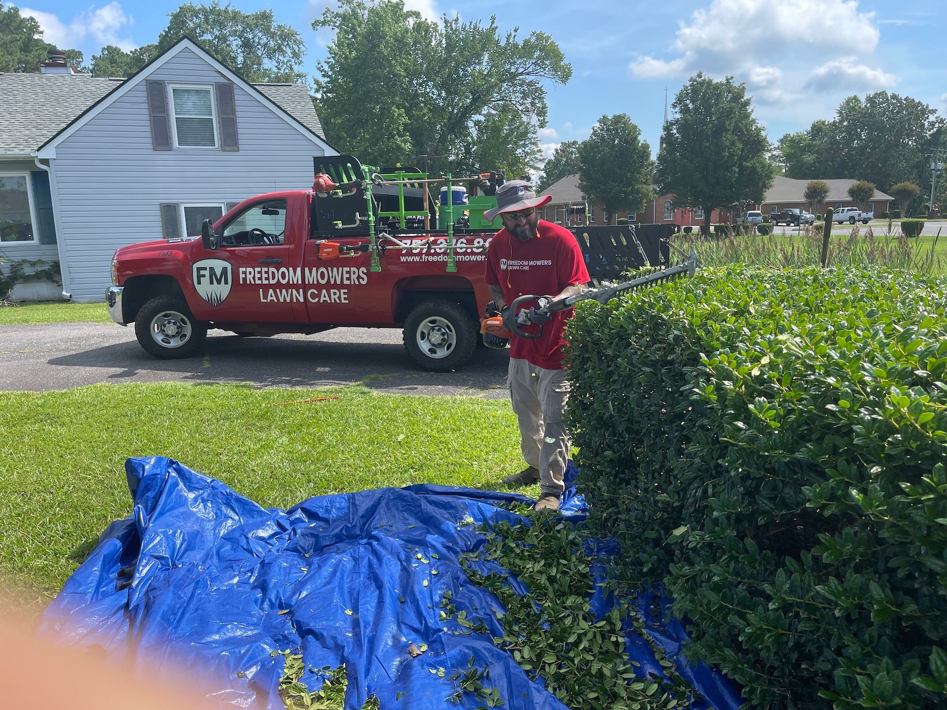 A man is cutting a hedge in front of a red truck.