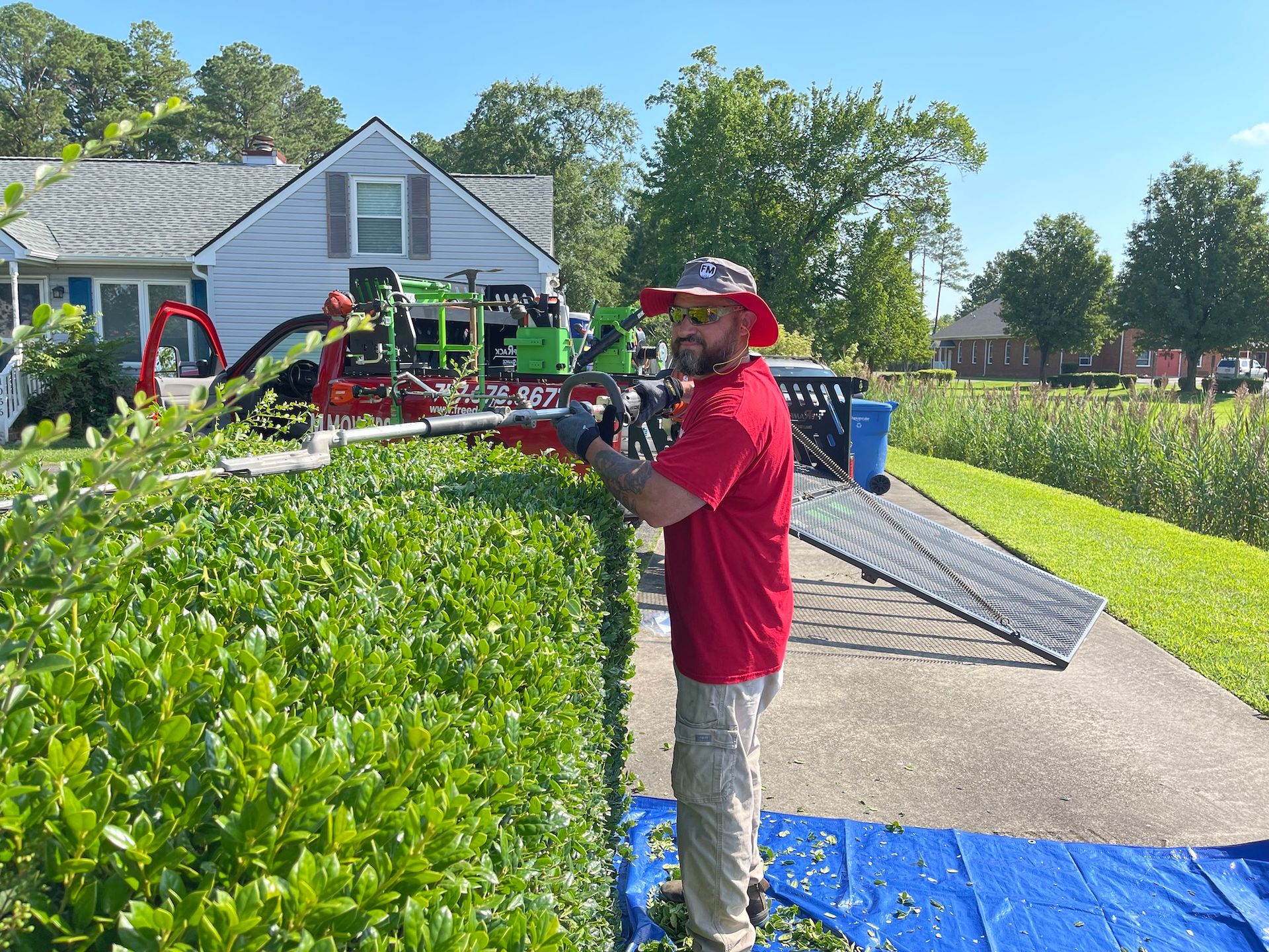 A man is cutting a hedge with a hedge trimmer in front of a house.