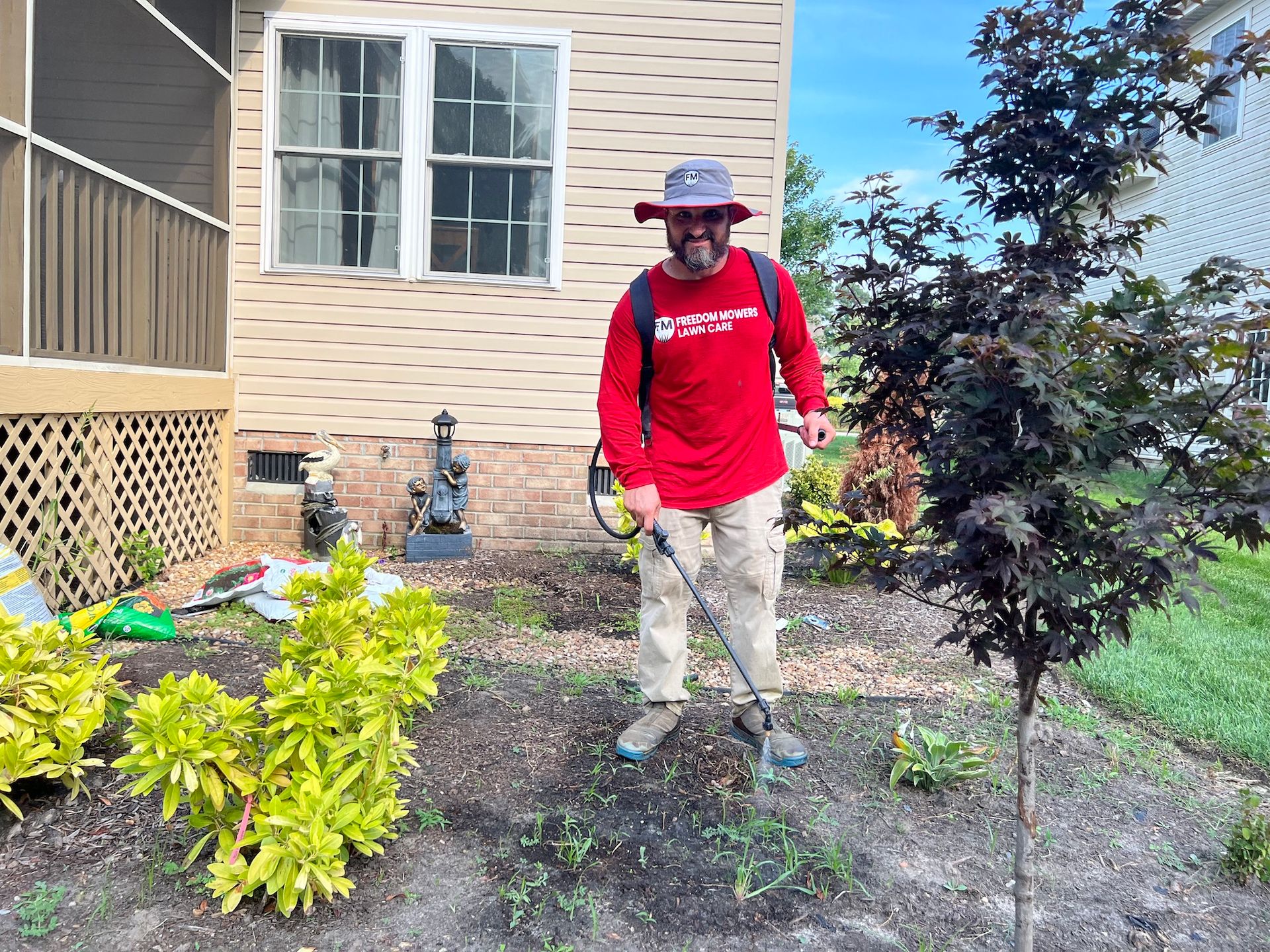 A man is standing in front of a house cutting grass with a lawn mower.