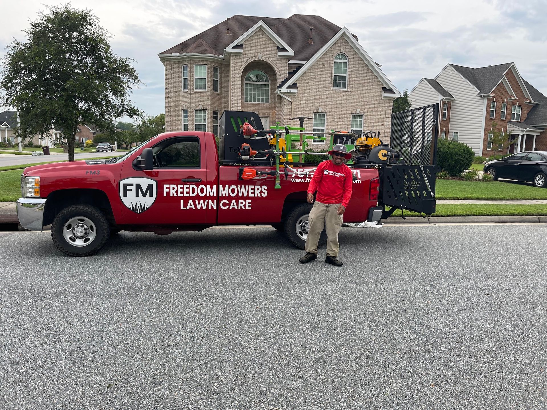 A man is standing next to a red truck that says freedom mowers lawn care.