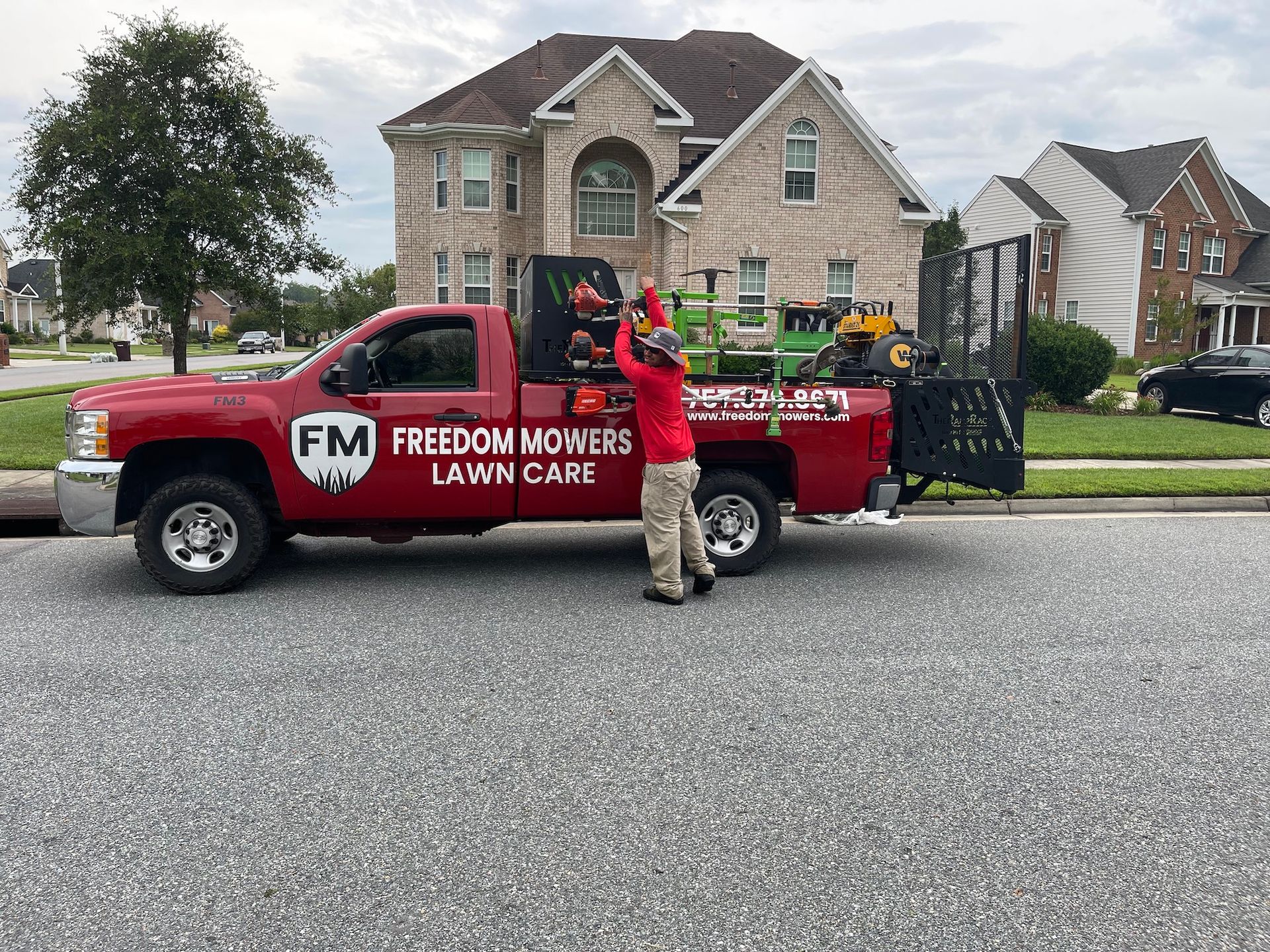 A man is standing next to a red truck that says freedom mowers lawn care.