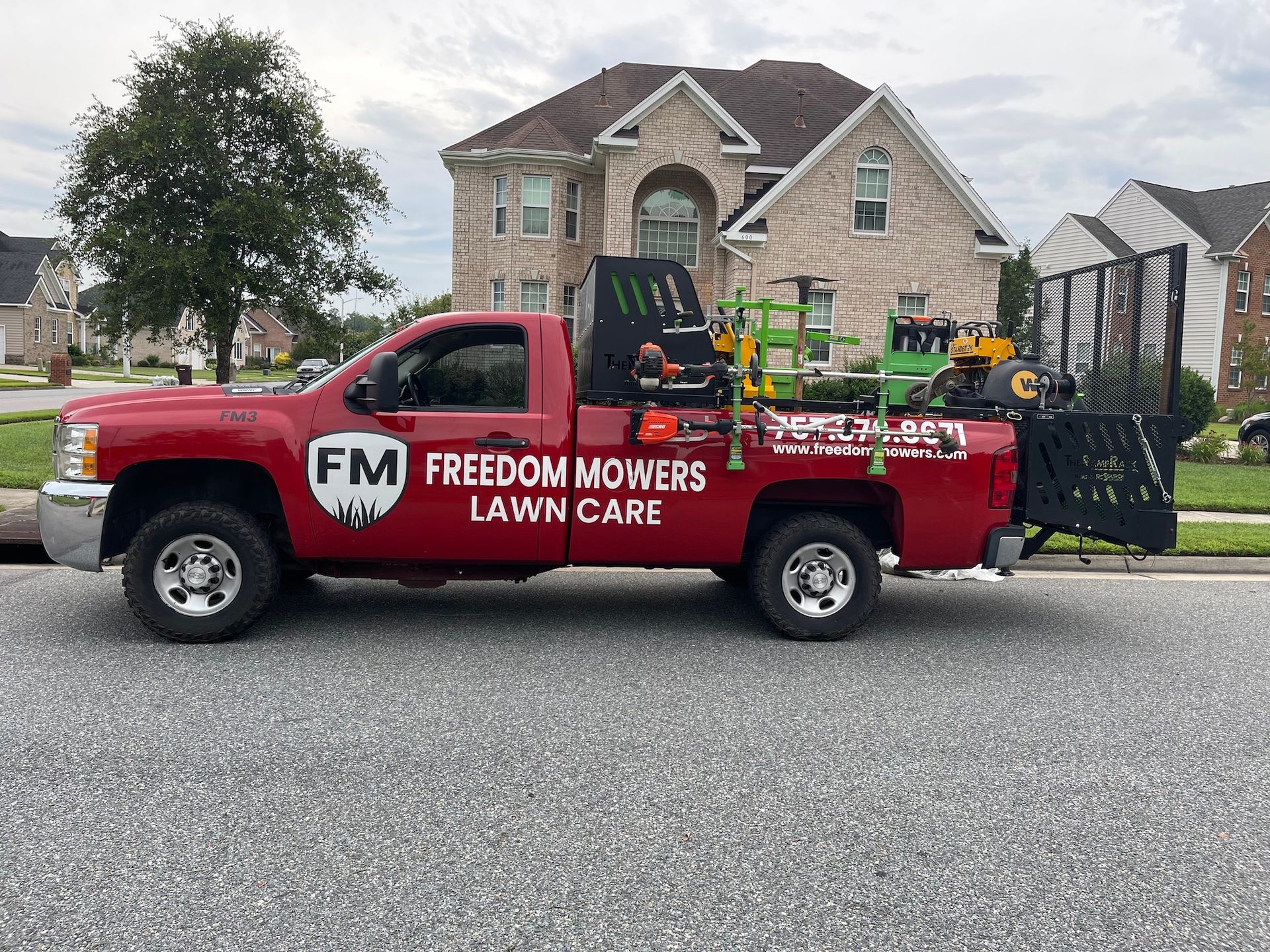 A red freedom mowers lawn care truck is parked in front of a house.