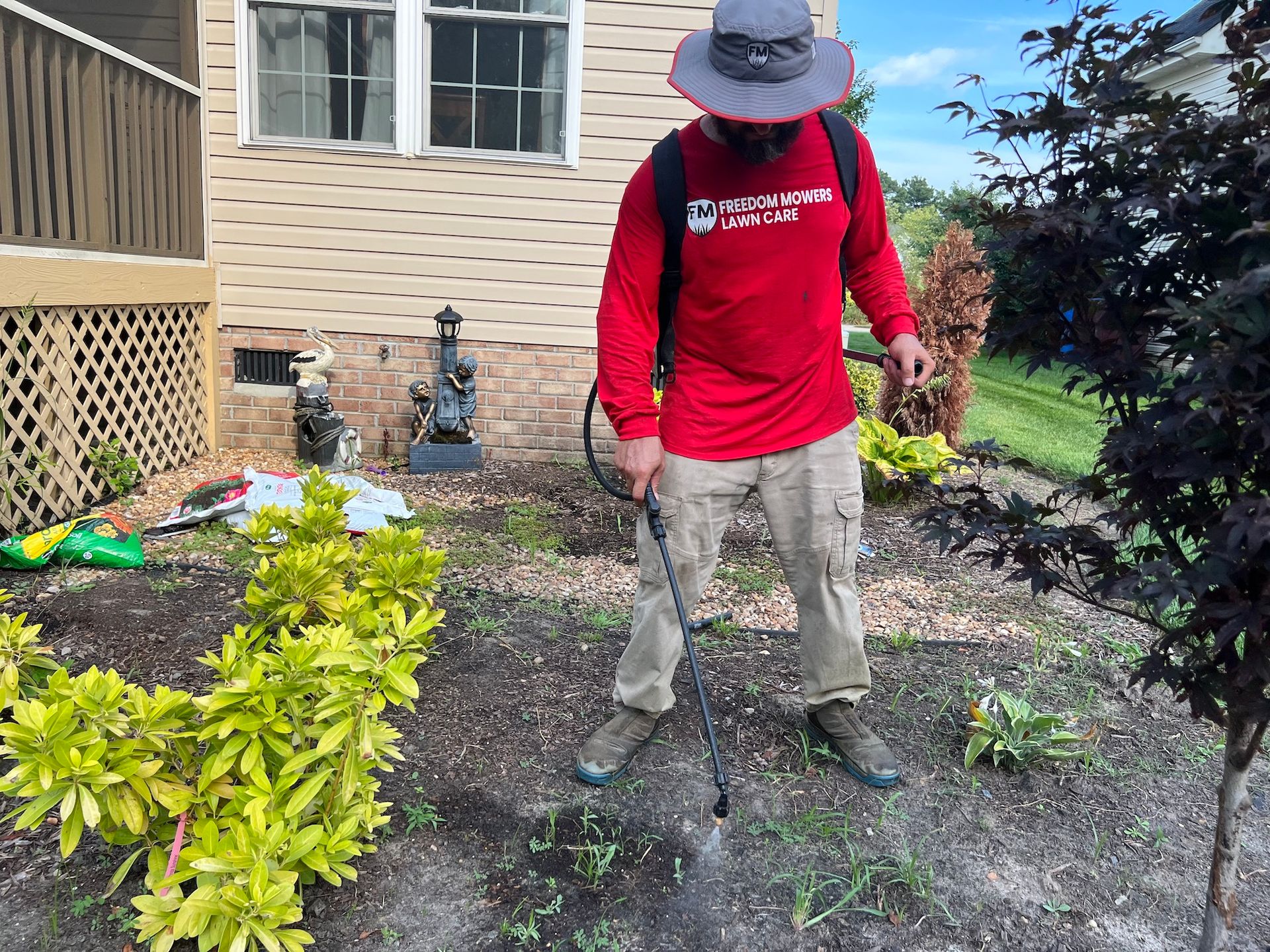 A man in a red shirt is spraying weeds in a garden.