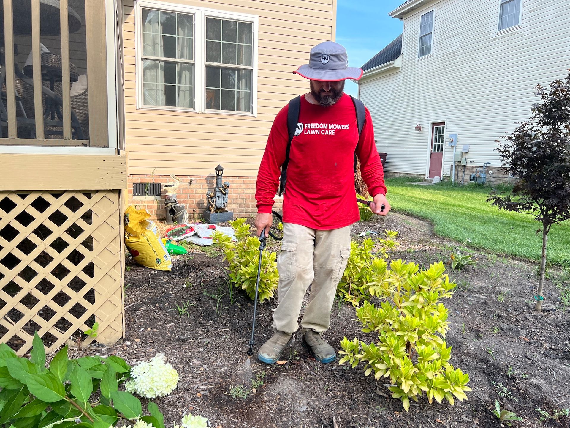 A man in a red shirt and hat is spraying plants in a garden.