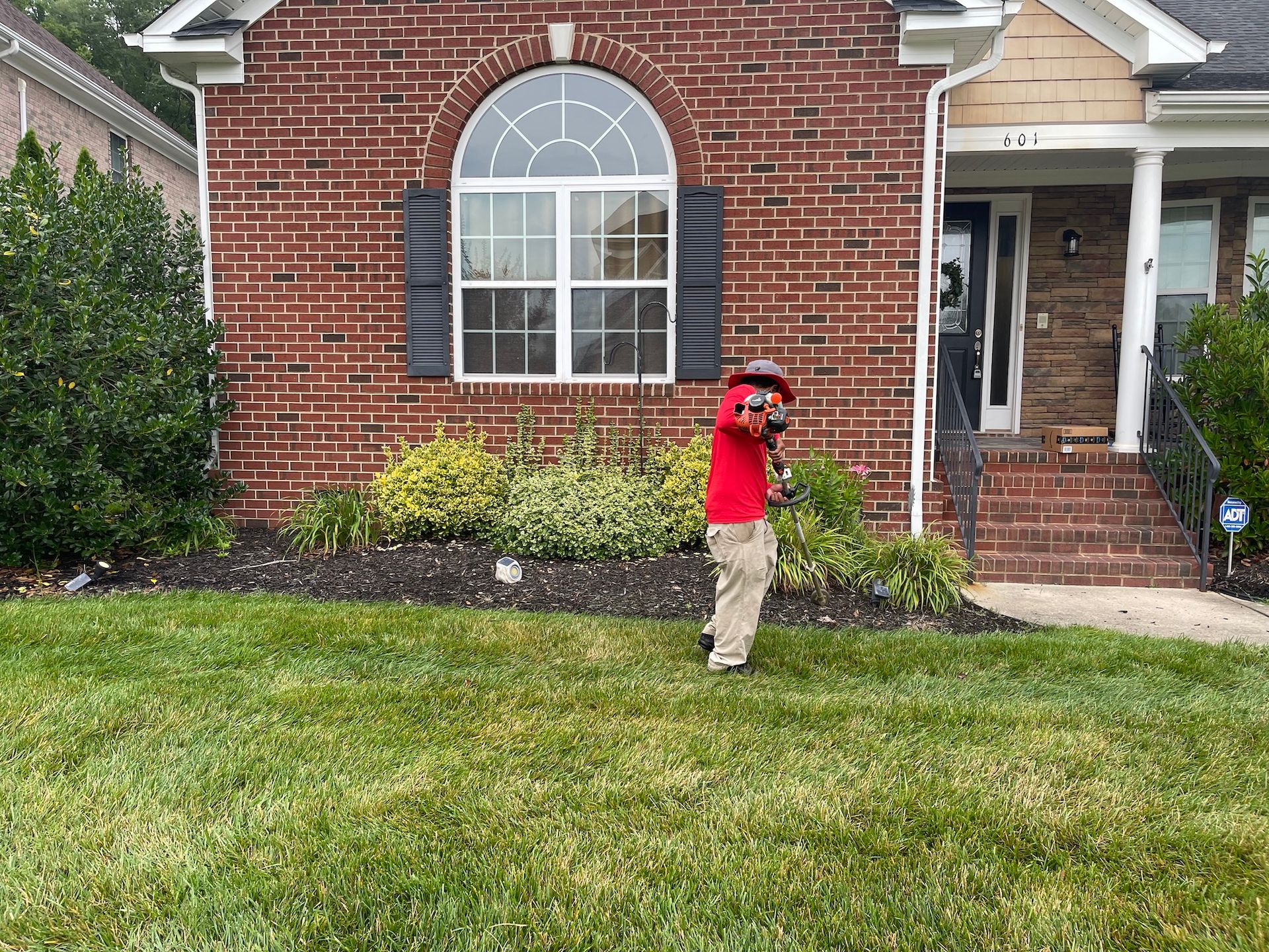 A young boy is standing in the grass in front of a brick house.