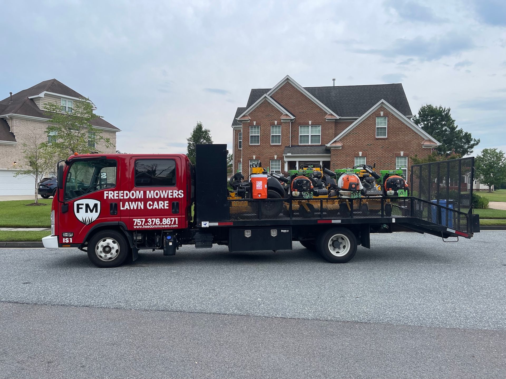 A red lawn care truck is parked in front of a brick house.