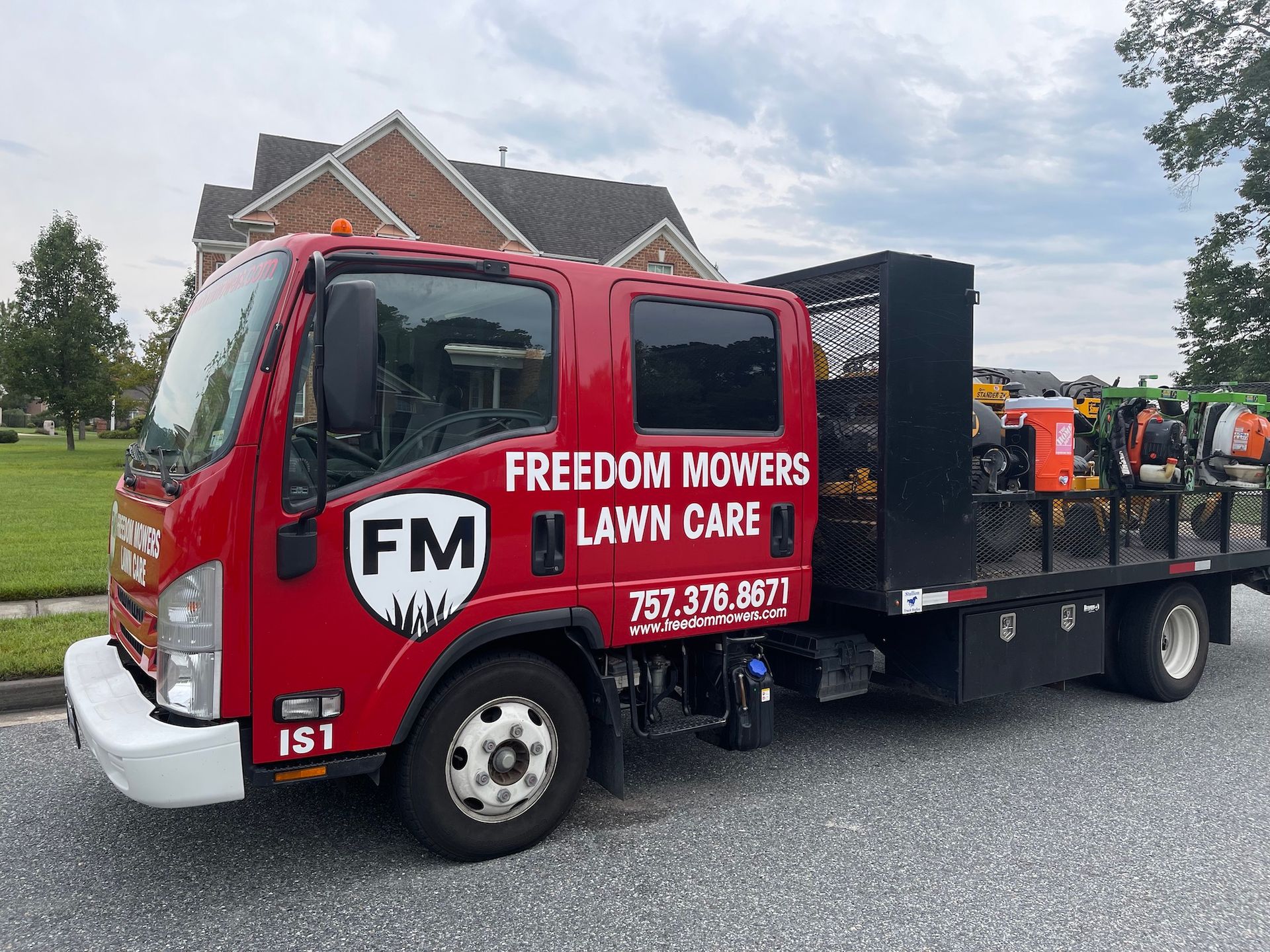 A red freedom mowers lawn care truck is parked in front of a house.