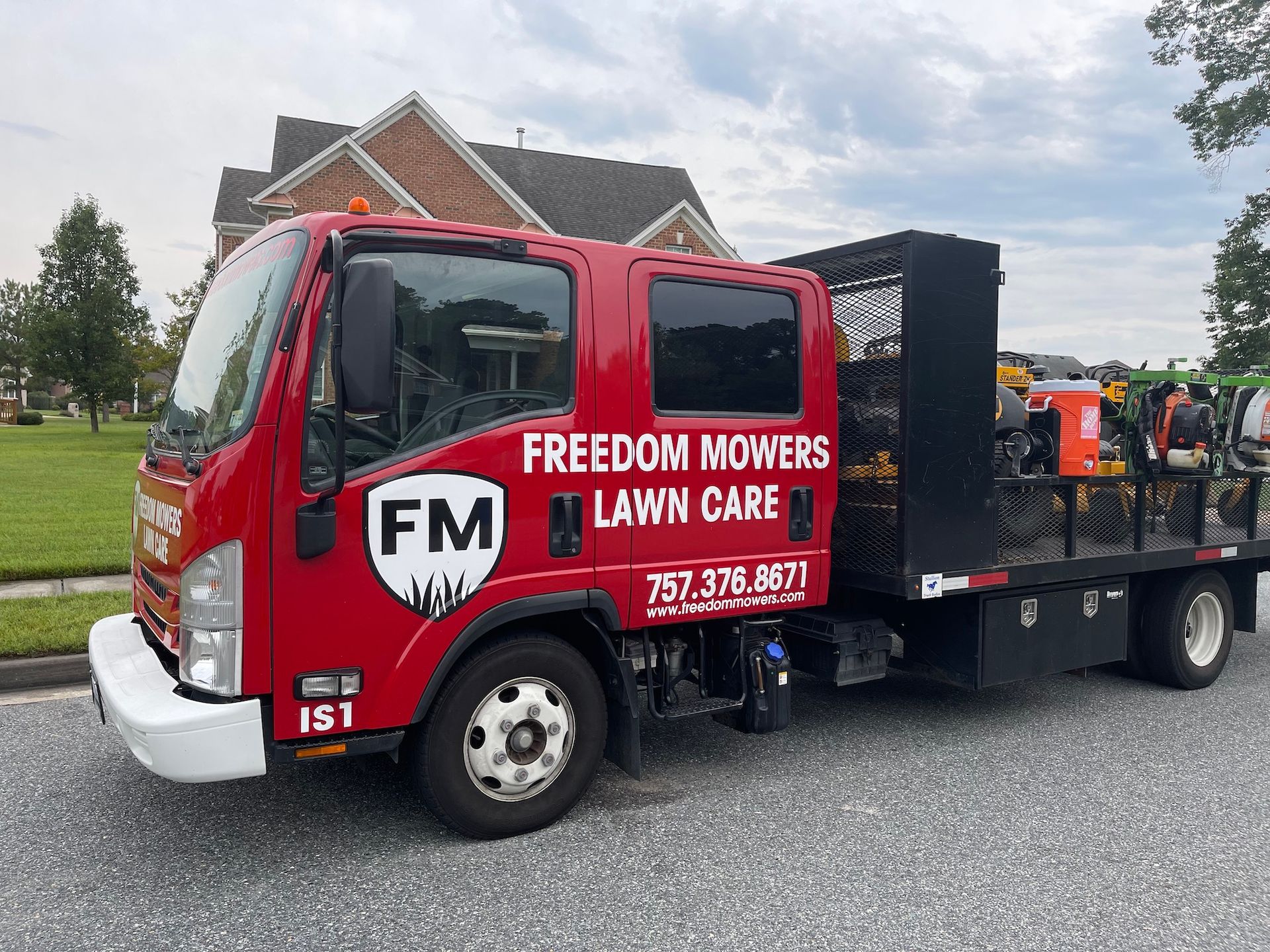 A red freedom mowers lawn care truck is parked on the side of the road.
