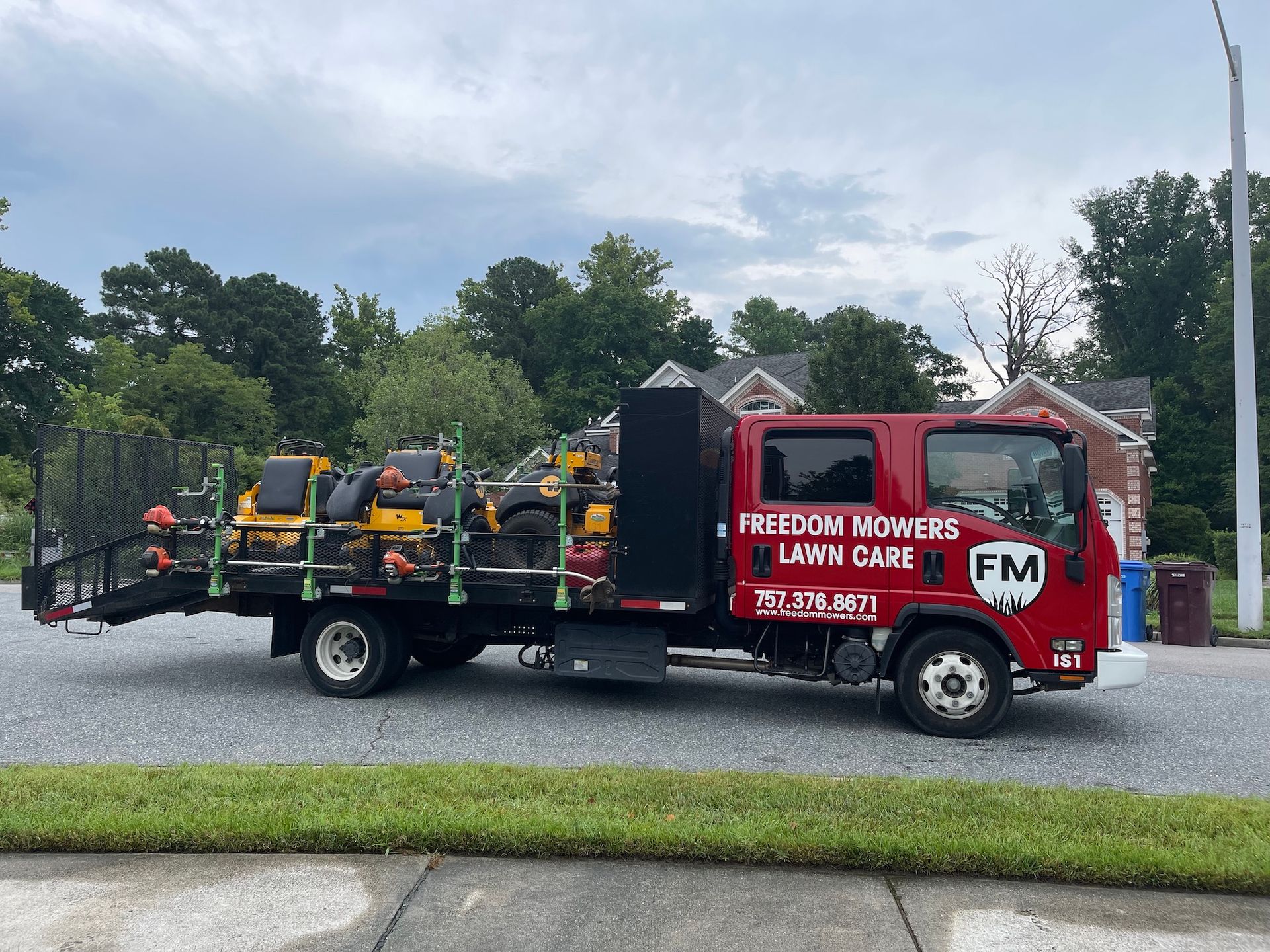 A red truck with lawn mowers on the back is parked on the side of the road.