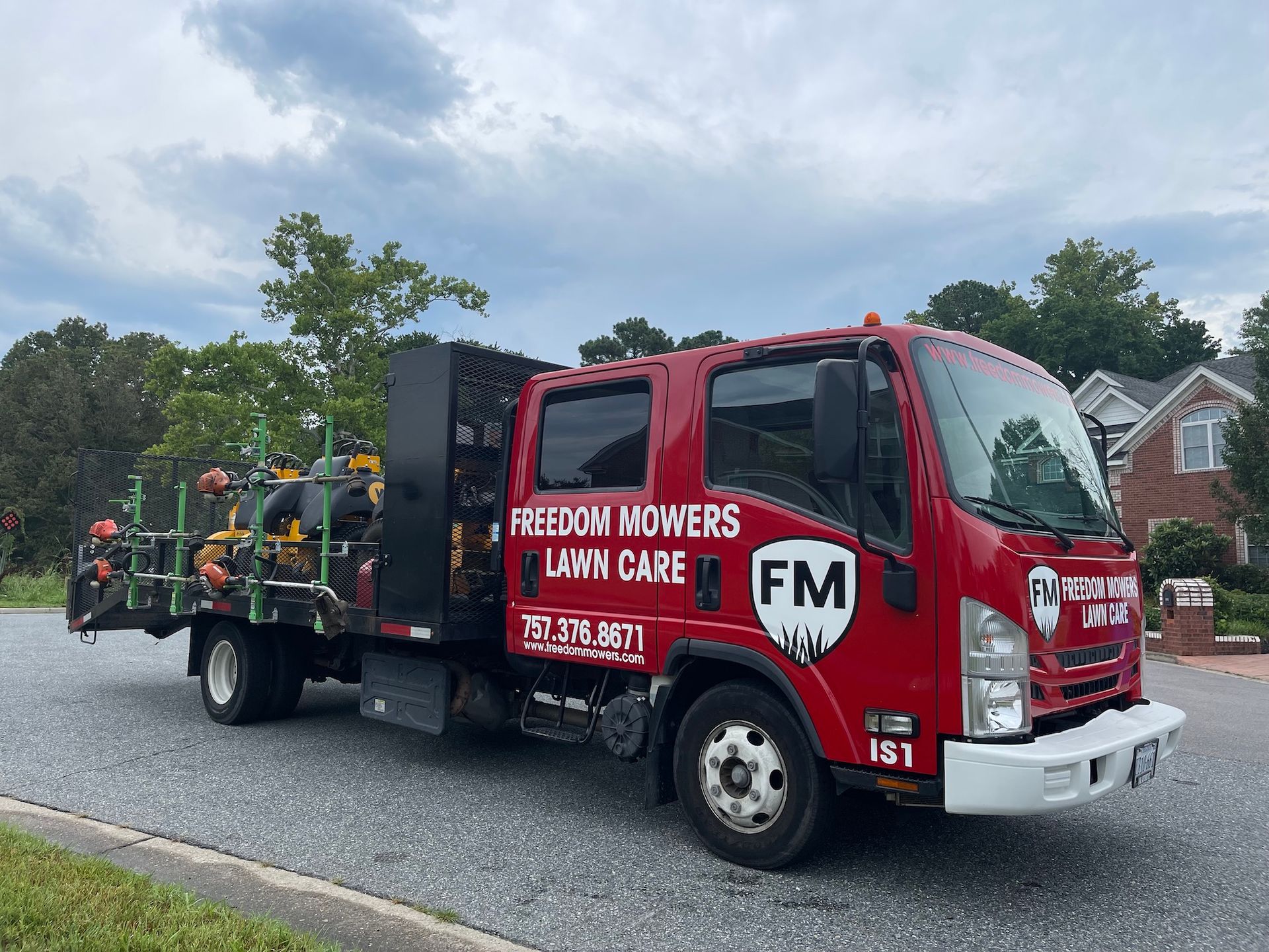 A red truck with lawn mowers on the back is parked on the side of the road.