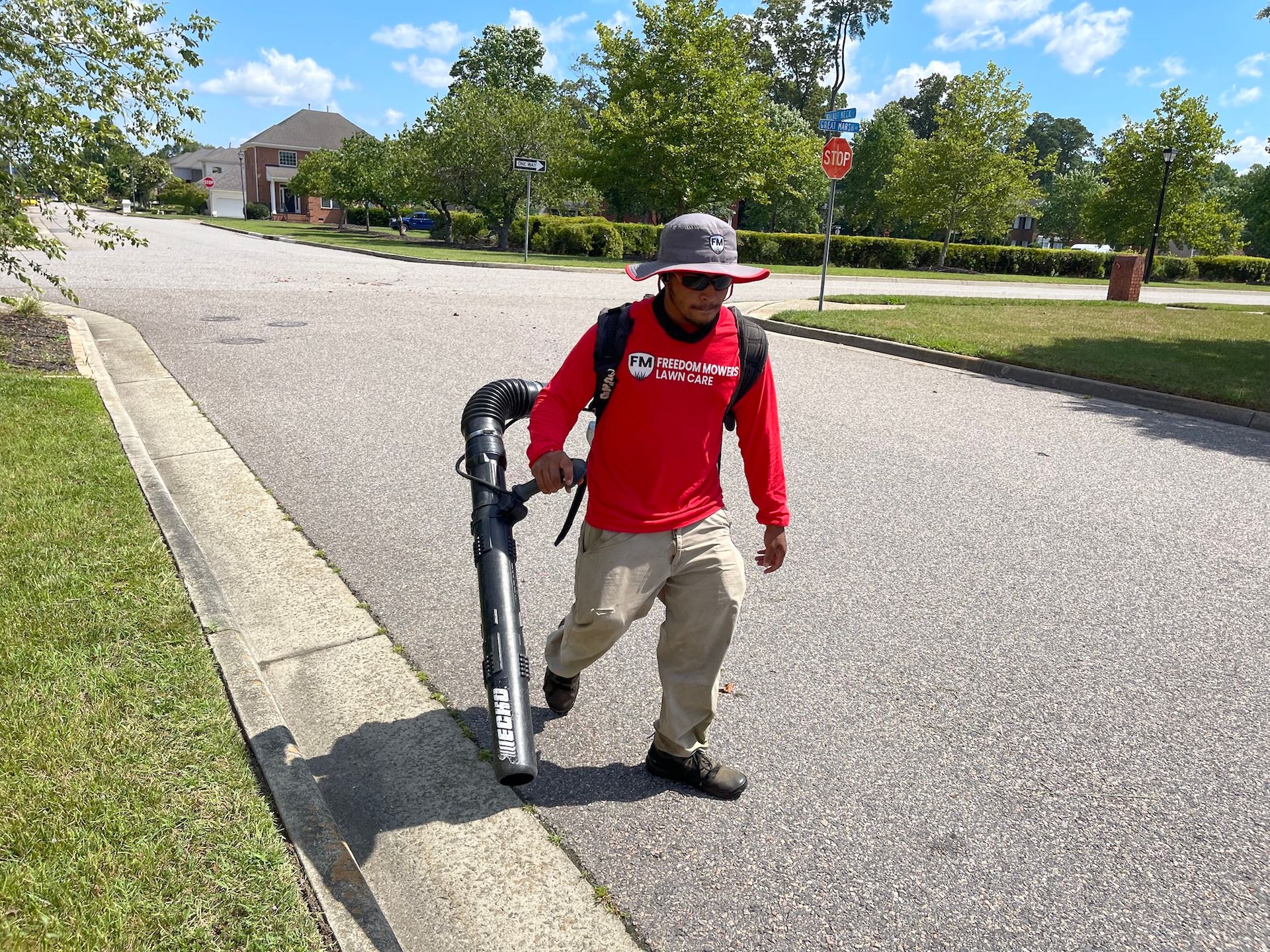 A man is walking down the sidewalk holding a blower.